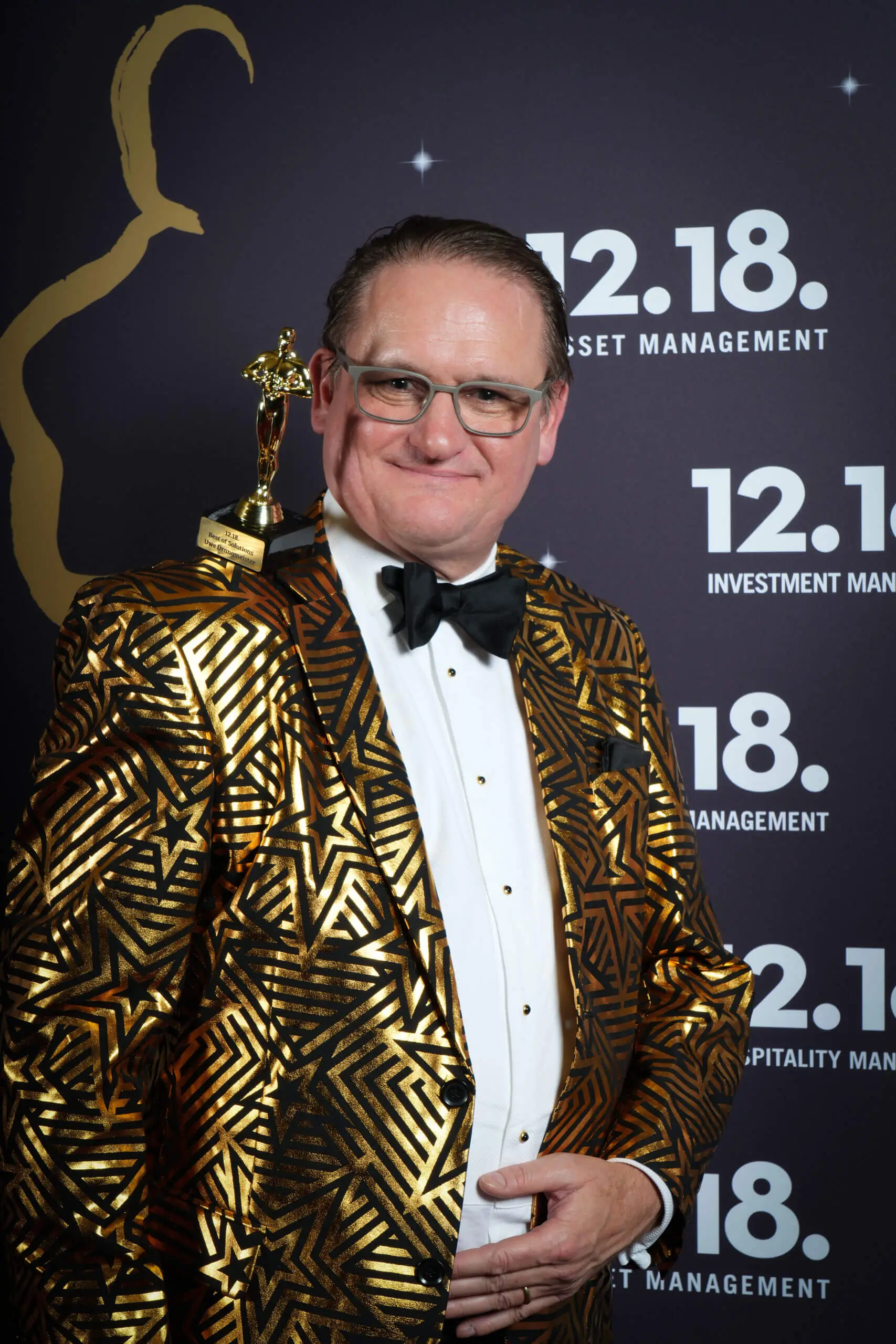 Mann im goldenen Anzug mit einer Auszeichnung, der vor einem Hintergrund für Investmentmanagement posiert.