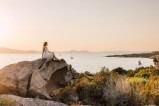 Frau sitzt auf einem Felsen mit Blick auf einen See im Freien, Symbol für überwältigende Gastfreundschaft