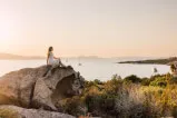 Frau sitzt auf einem Felsen mit Blick auf einen See im Freien, Symbol für überwältigende Gastfreundschaft