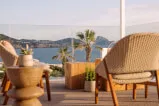 A chair and table placed outdoors with a view of the water and mountains in the background owned by 12. 18. Investment Management GmbH.