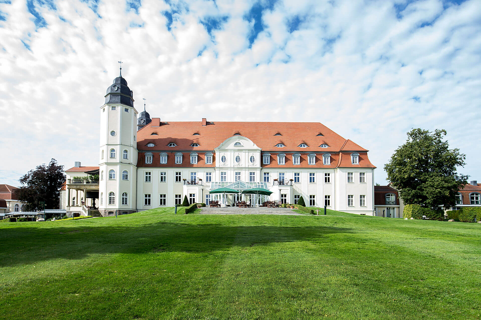 A spacious white building with a vast lawn and Wieskirche in the background