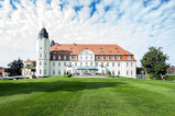 A spacious white building with a vast lawn and Wieskirche in the background
