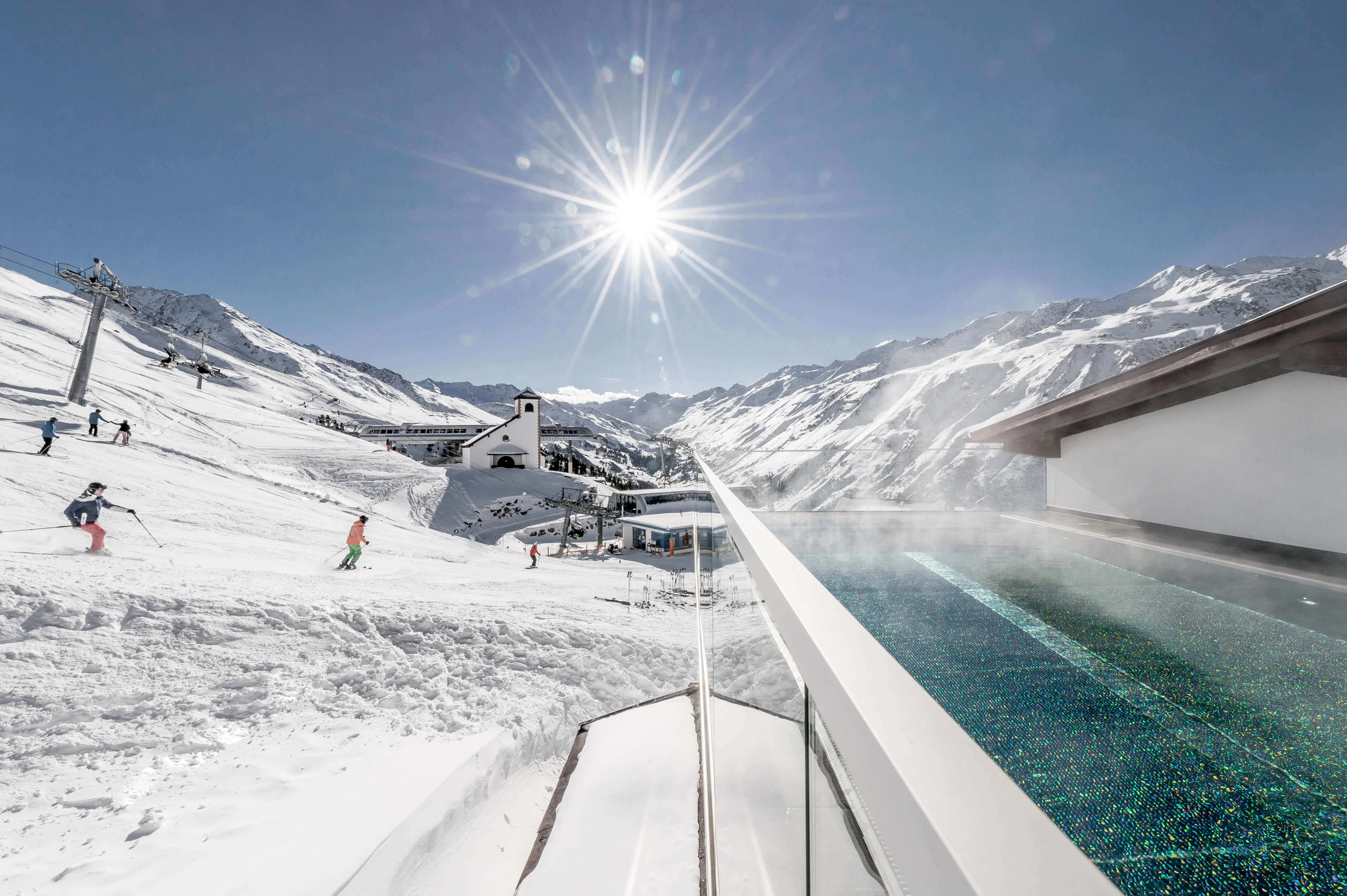 Skiresort mit Pool in den Bergen und Sonnenstrahlen bei klarem Himmel.