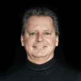A man wearing a black turtleneck standing in front of a blurred background. Image related to 12. 18. Investment Management GmbH website.