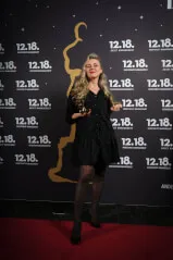 A woman in a black dress holding a trophy with 12. 18. Investment Management GmbH as the background context.