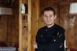 Mann in schwarzem Mantel lächelt in Innenraum, symbolisiert Service in touristischen Immobilien