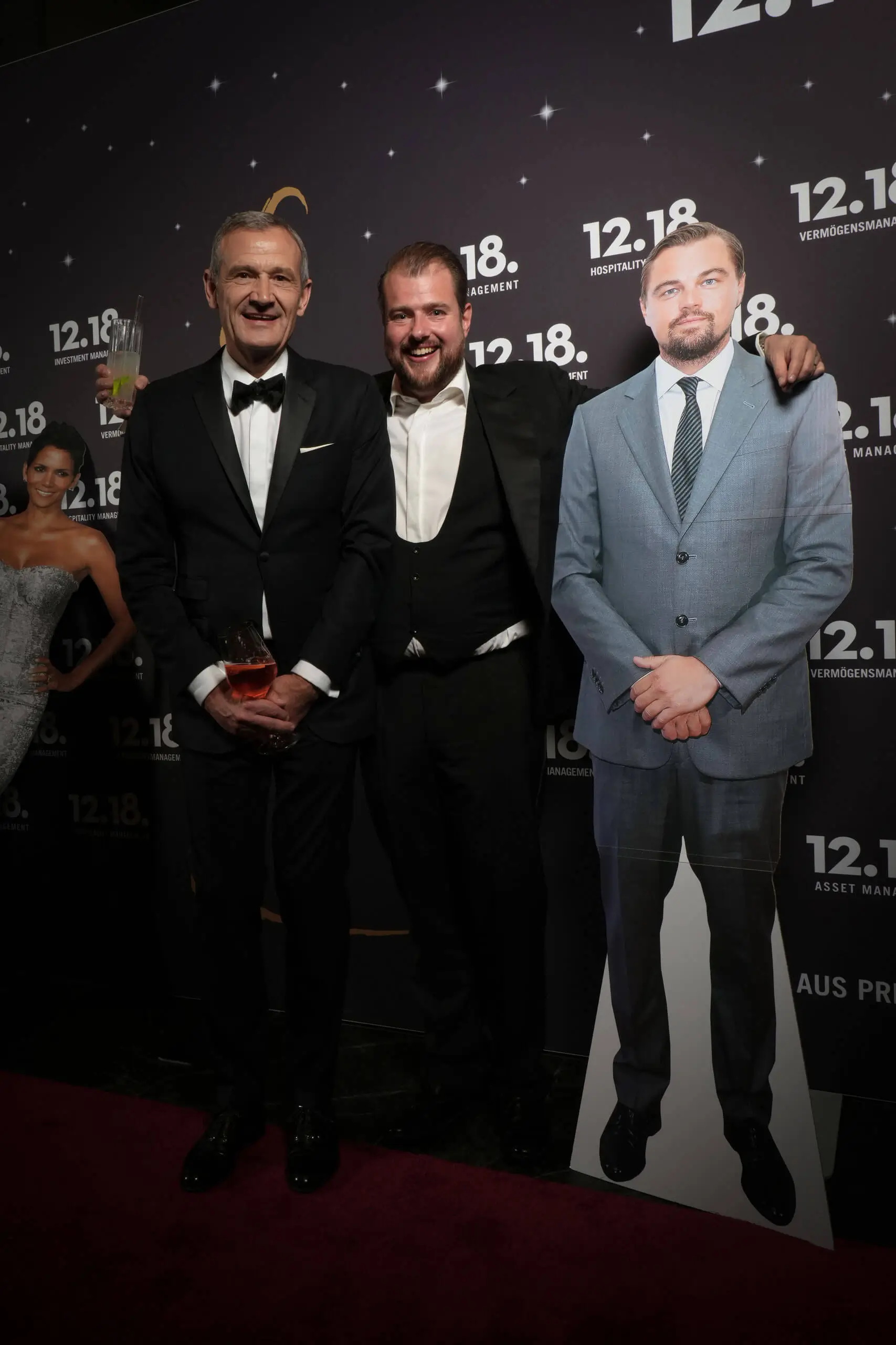 Zwei Männer bei einer Veranstaltung, einer im Smoking und ein Pappaufsteller von Leonardo DiCaprio.