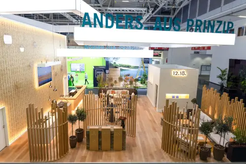 Modernes Ausstellungsstand mit Holzdekoration, digitalen Displays und Pflanzen.