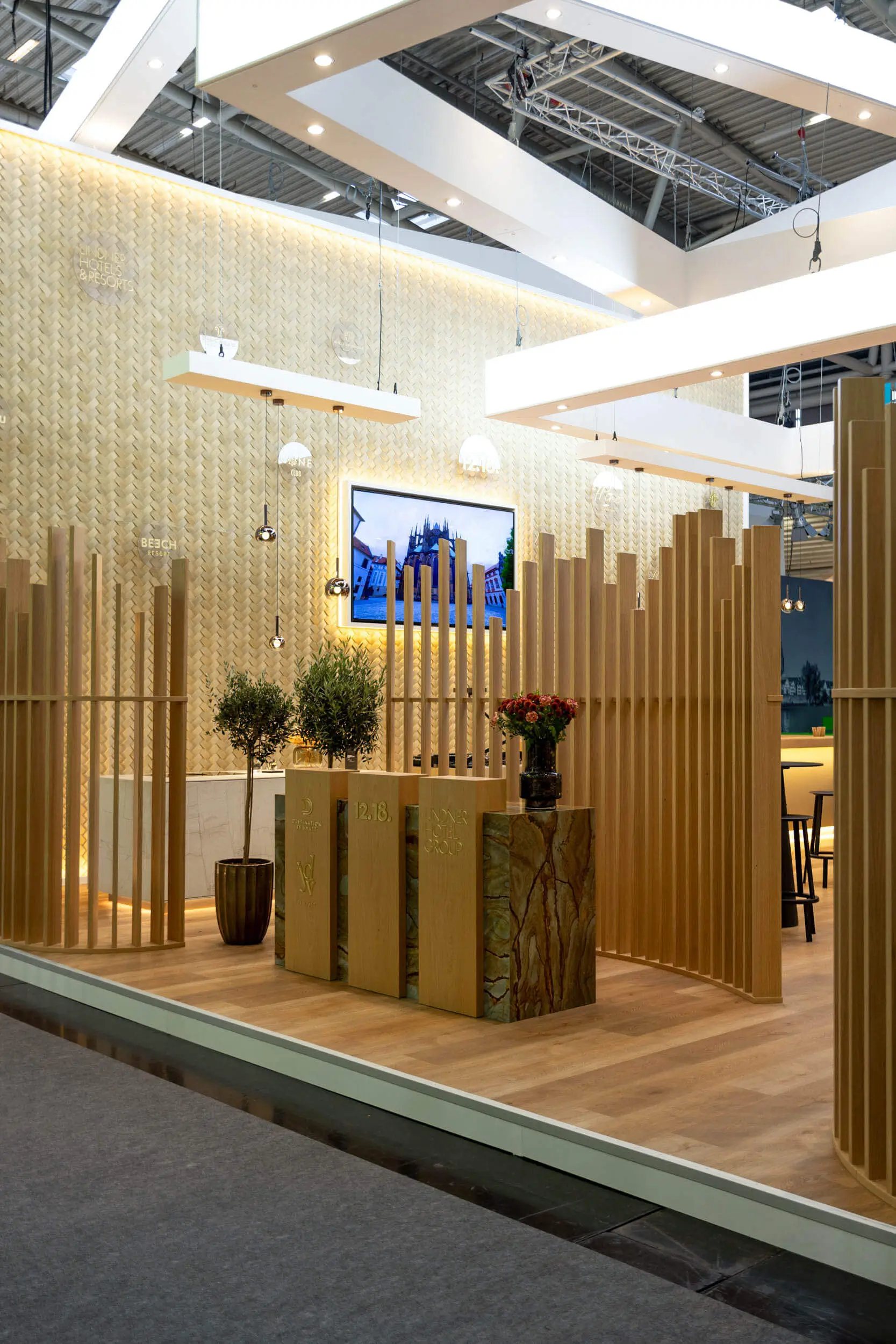 Moderner Messestand mit Holzlamellen, Pflanzen und beleuchtetem Bildschirm.