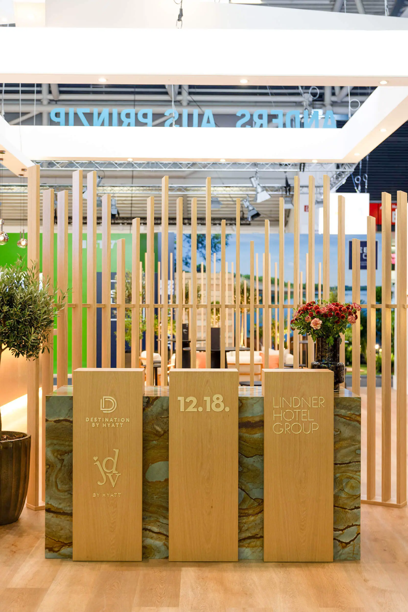 Messestand mit Holzpaneelen, Blumenarrangement und Markenlogos von Lindner Hotel Group und Destination by Hyatt.