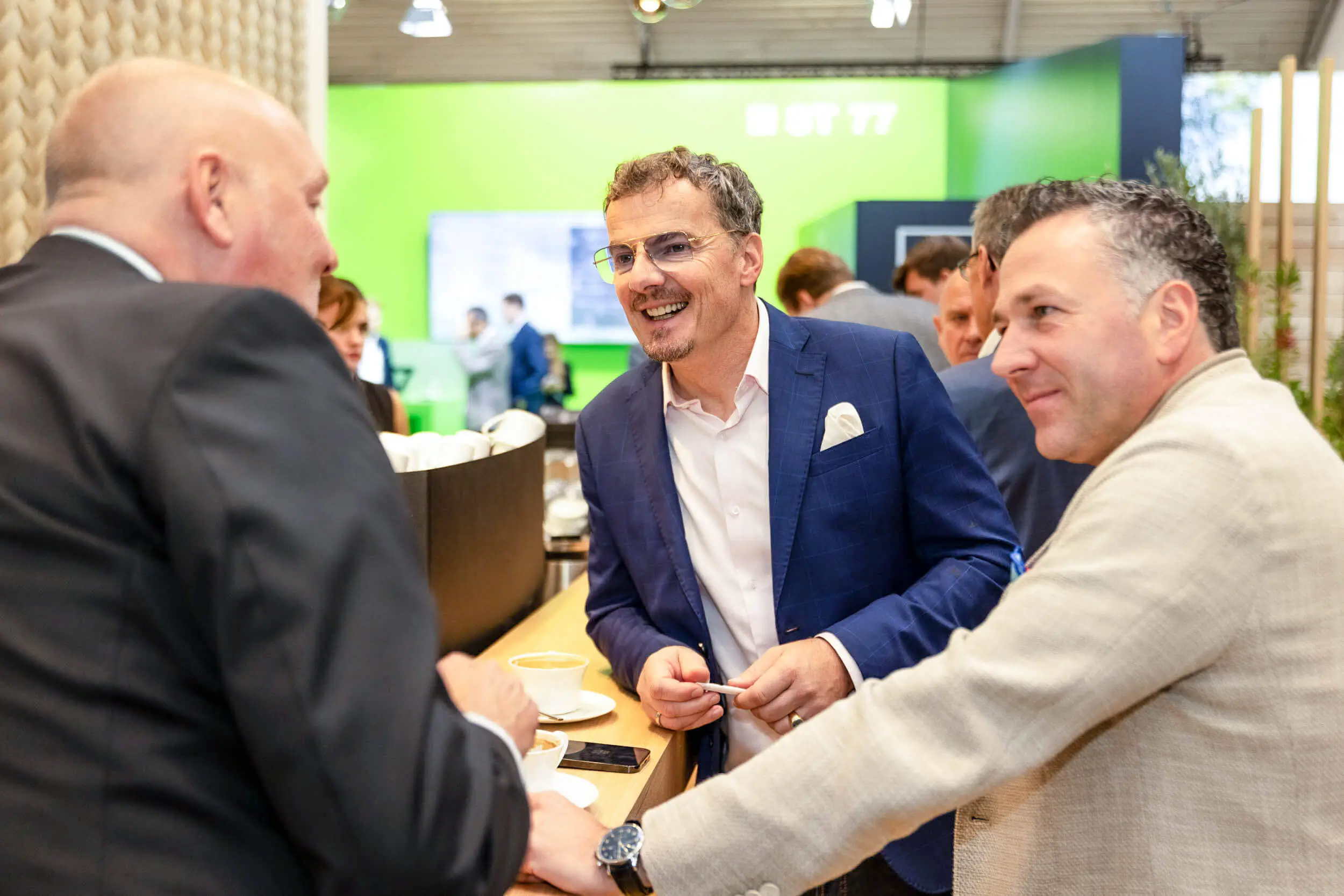 Drei Fachleute unterhalten sich bei Kaffee an einem Messestand.