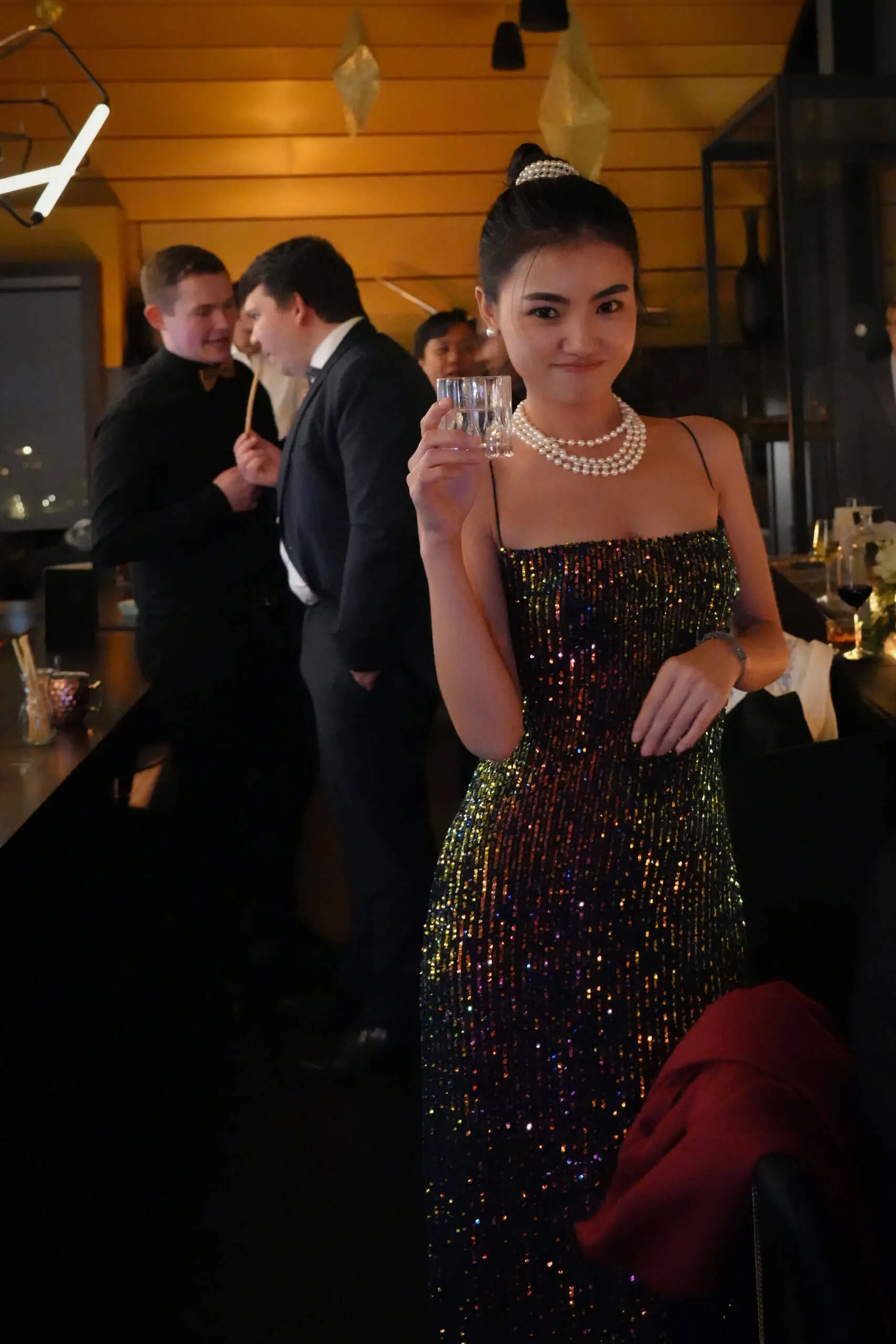 Glamouröse Frau in einem Paillettenkleid, feiernd mit Freunden in einer stilvollen Bar.