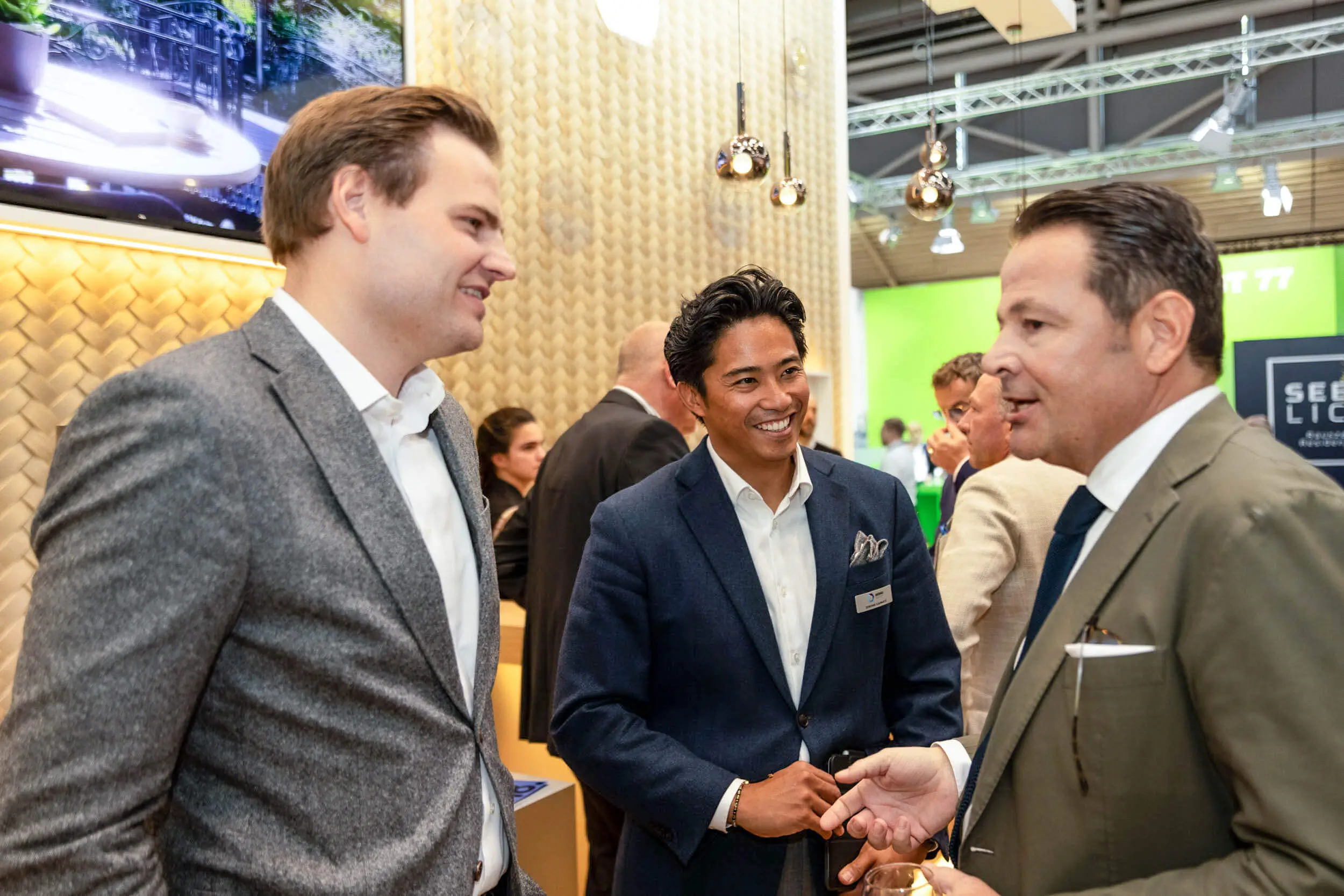 Drei Männer im Anzug sprechen an einem Messestand.