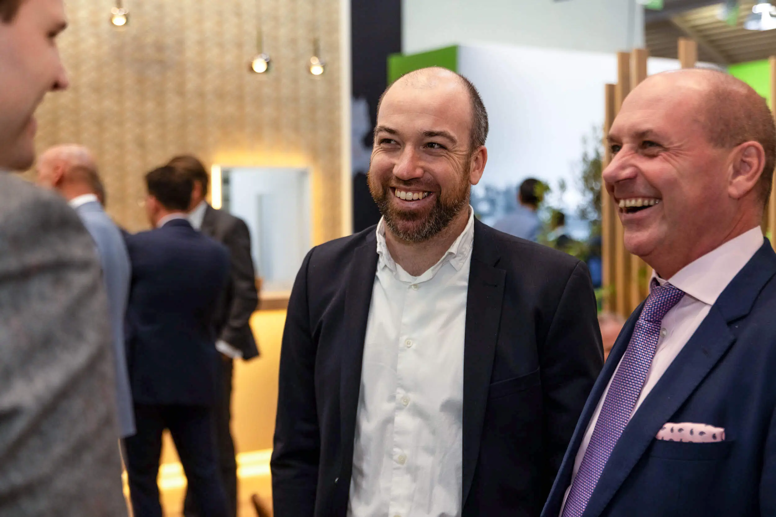 Zwei Männer im Anzug lachen und unterhalten sich auf einer Business-Veranstaltung.