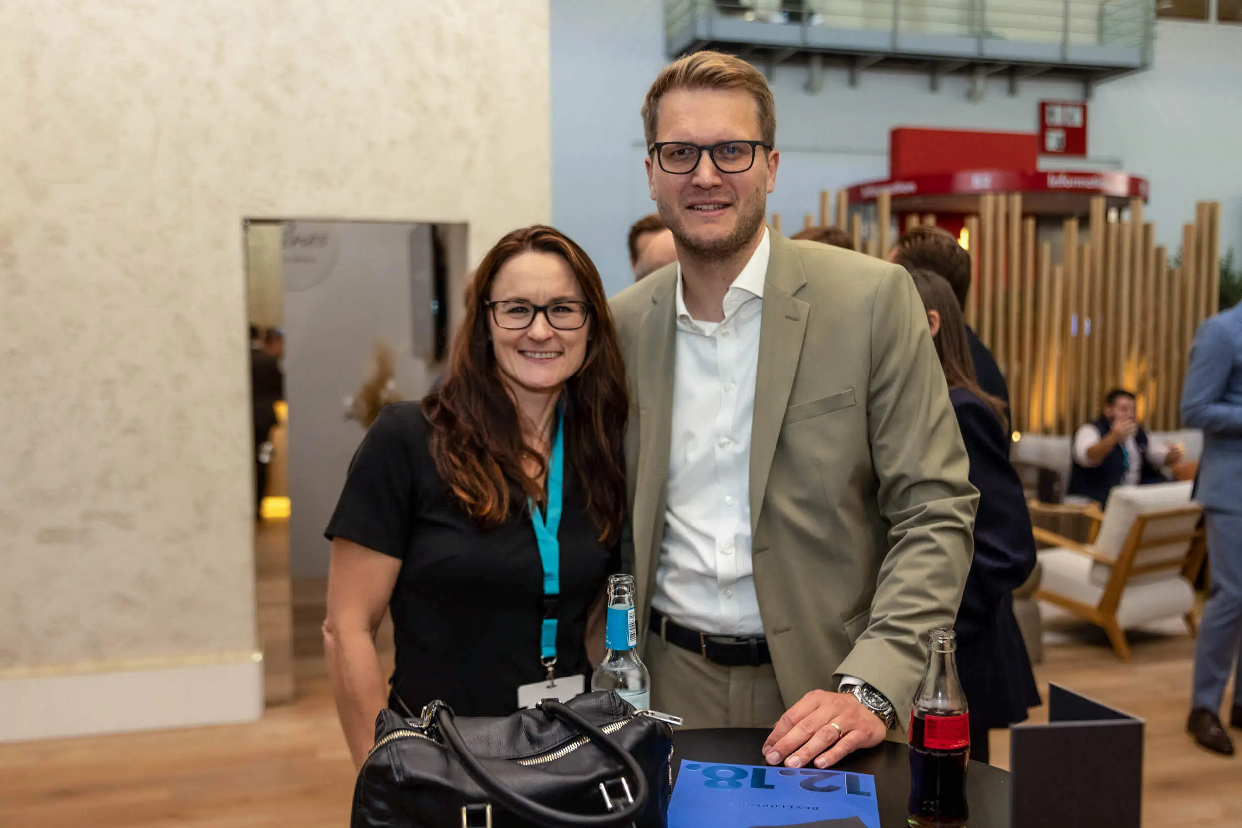 Zwei Fachleute lächeln auf einer Messeveranstaltung vor einem Stand.