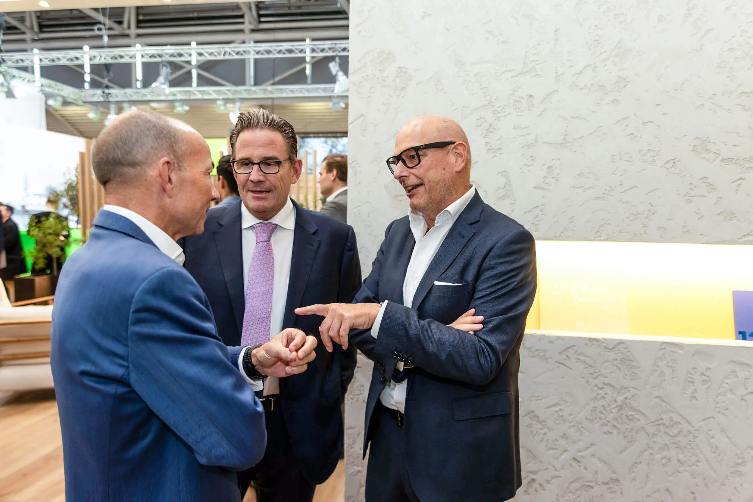 Drei Geschäftsleute unterhalten sich an einem Messestand.