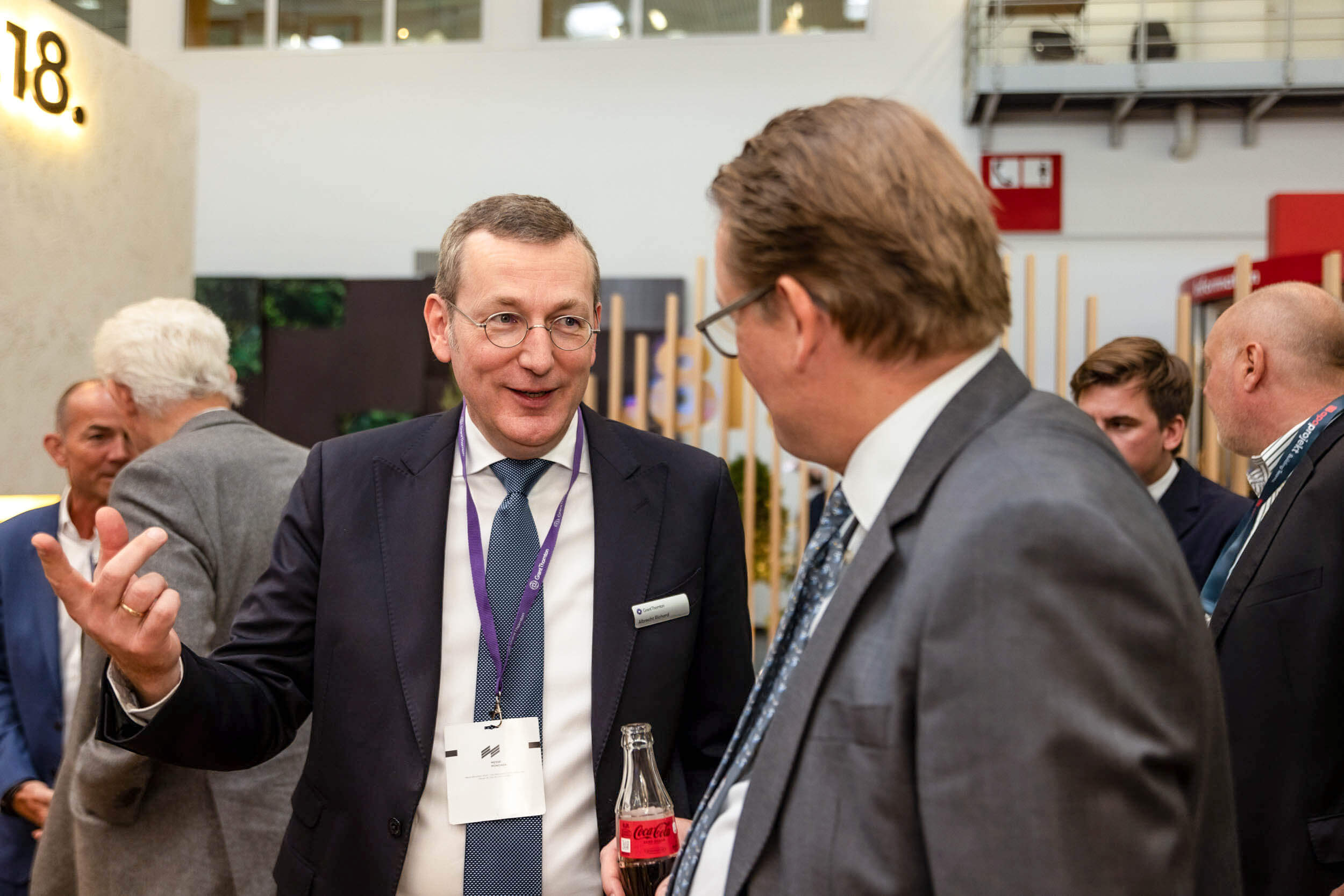 Zwei Geschäftsleute unterhalten sich auf einer Fachmesse, mit einer sichtbaren Coca-Cola-Flasche.