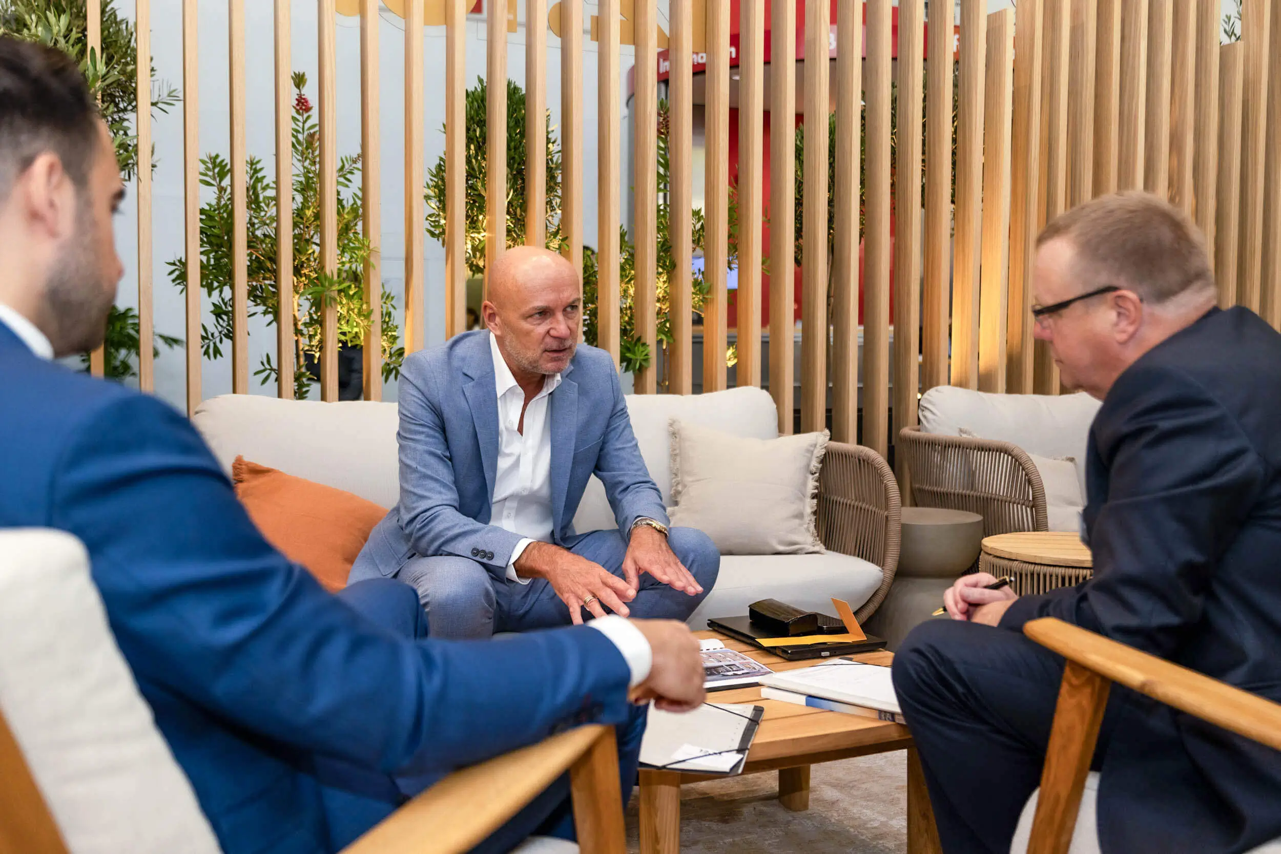 Drei Fachleute besprechen ein Projekt in einer modernen Lounge mit Holzlamellen und Pflanzen.