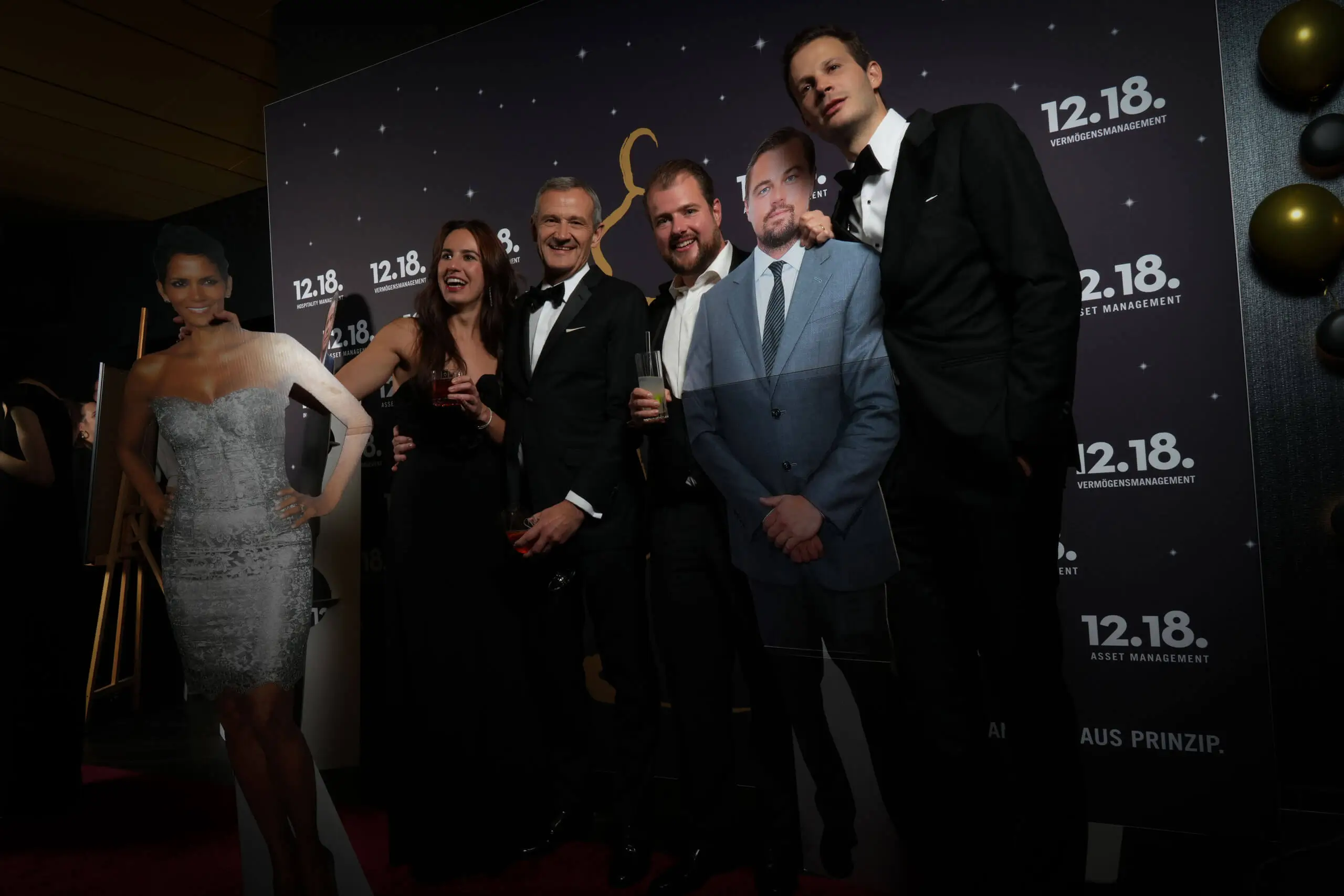 Gäste bei einer glamourösen Veranstaltung mit Star-Ausschnitten im Hintergrund.