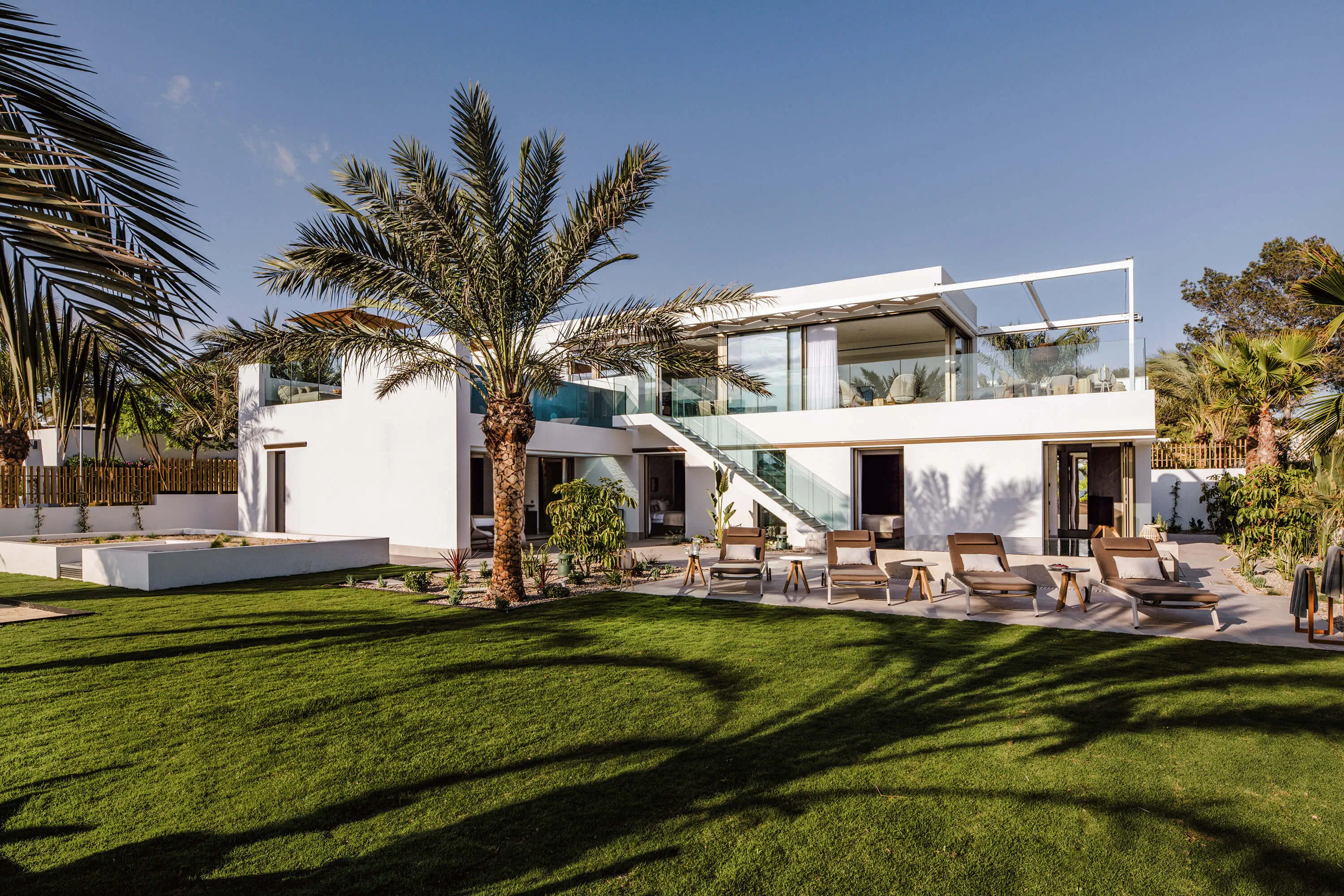 Moderne Villa mit Palmen und Liegen in einem sonnigen Garten.
