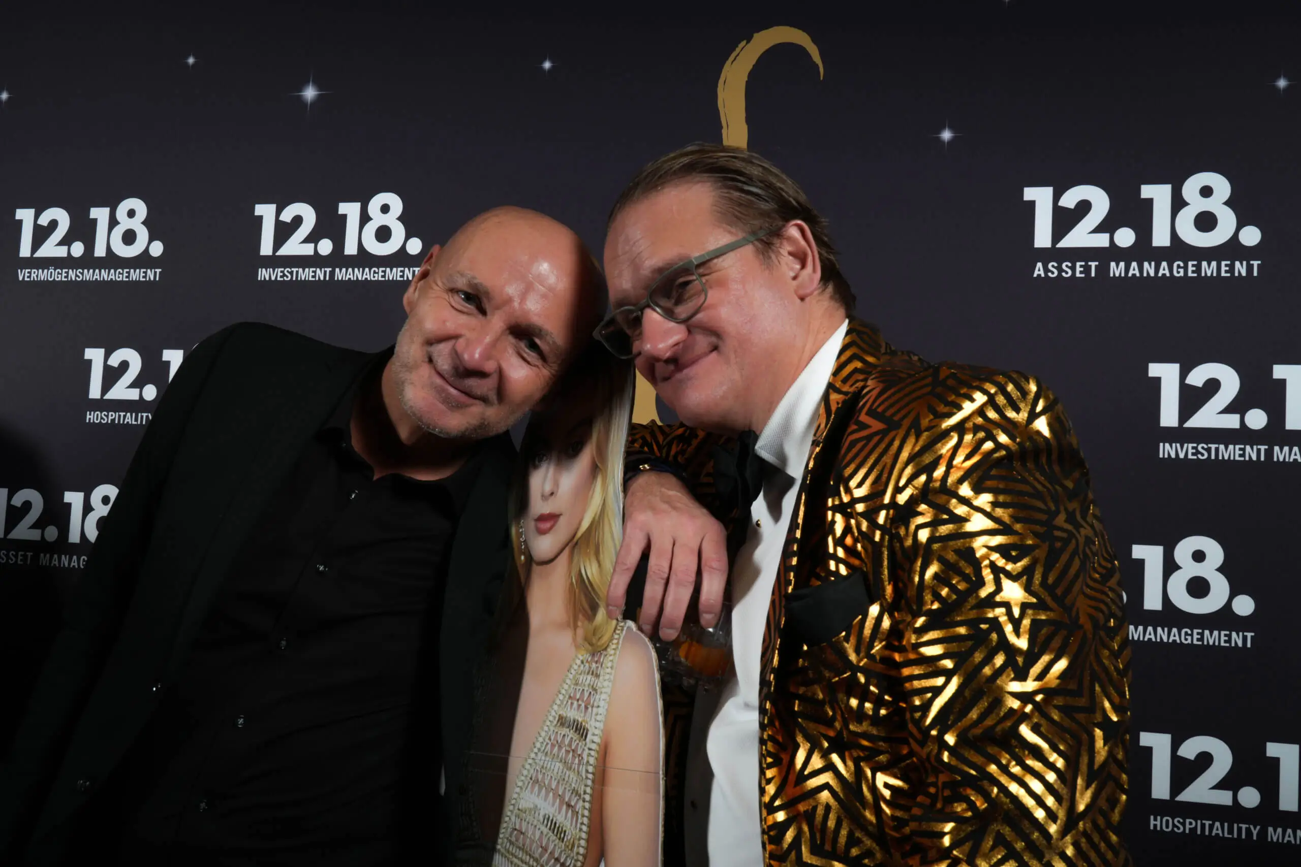 Zwei Männer mit einem glänzenden Jackett und einem Lächeln bei einem glamourösen Event.