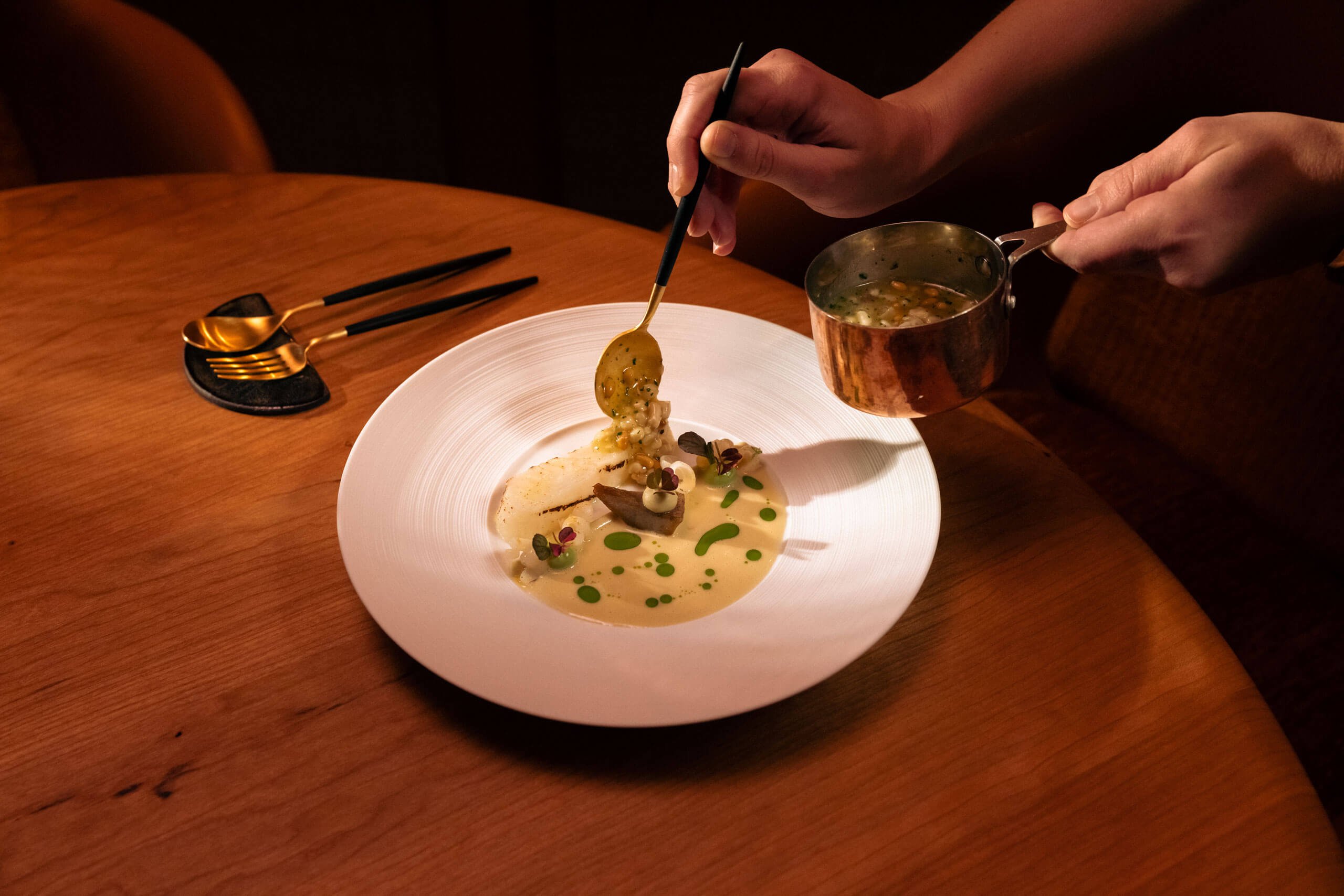 Eine Person hält einen Löffel über einem Teller mit Essen, der auf einem Esstisch serviert wird. 