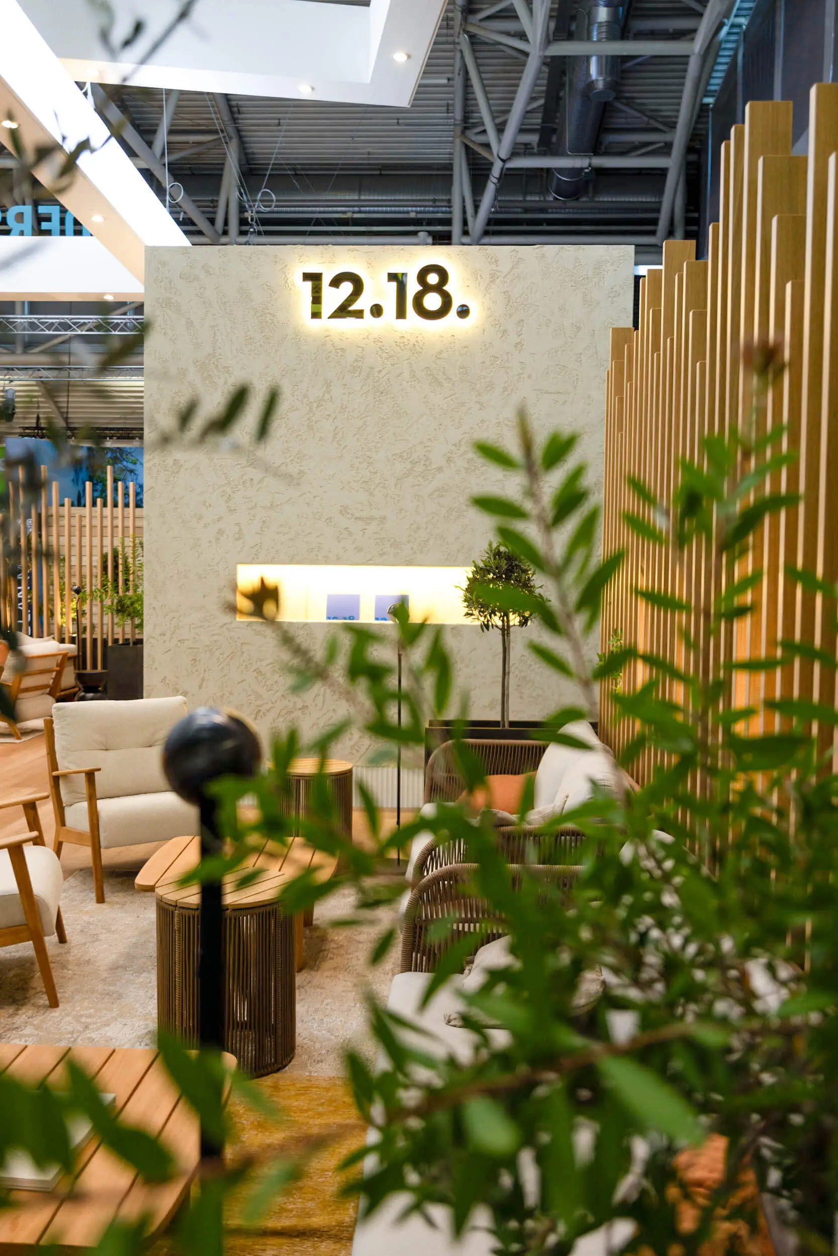 Stilvolle Lounge-Innenarchitektur mit beleuchtetem 12.18.-Wandschild, Sitzmöbeln, Pflanzen und Holztrennwänden.