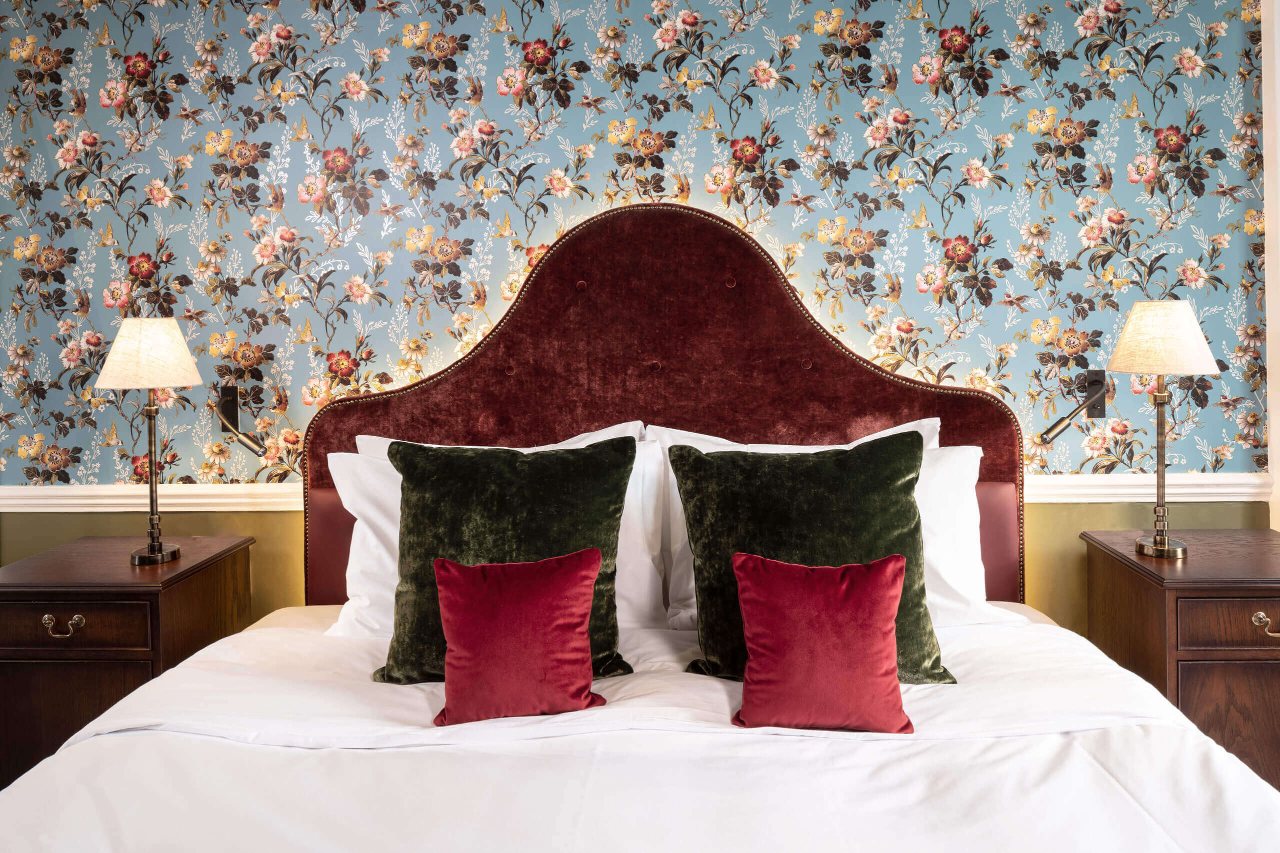 A bed with pillows and a floral wallpaper in a room