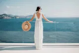 Frau in einem weißen Kleid, die einen Strohhut hält und an einem Geländer steht, symbolisiert elegante Freizeitkleidung in touristischen Immobilien