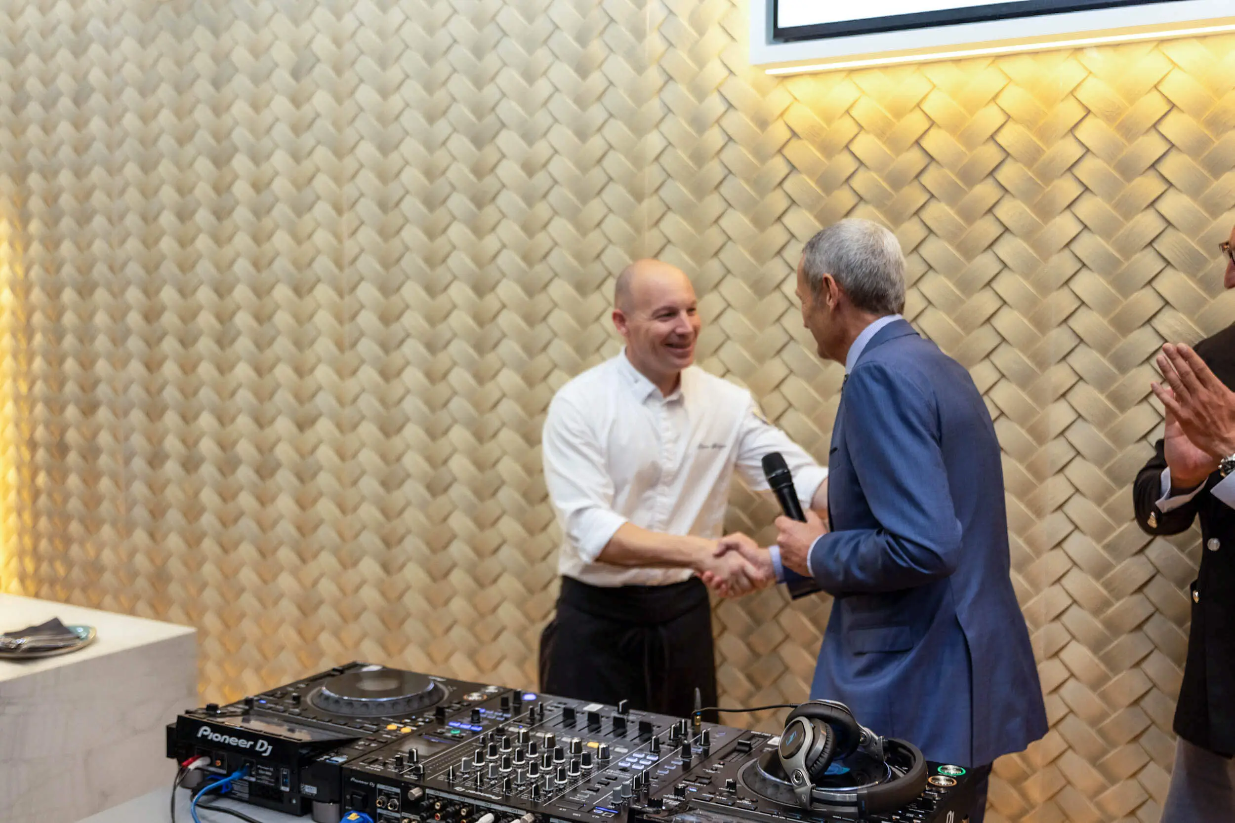 Zwei Männer begrüßen sich mit Handschlag vor DJ-Equipment bei einer Veranstaltung.