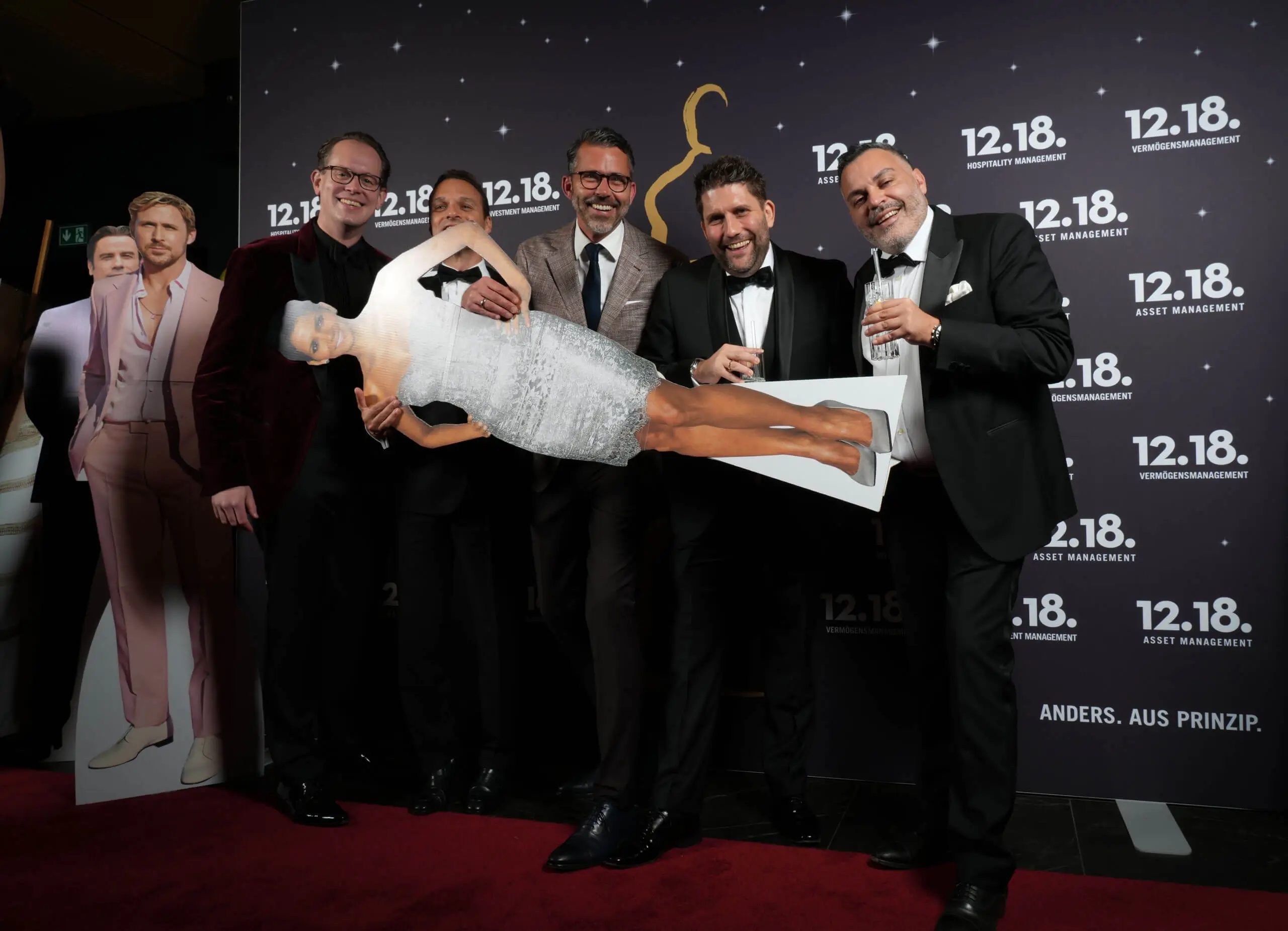 Eine Gruppe von Männern hält einen lebensgroßen Pappaufsteller einer Frau in einem funkelnden Kleid.