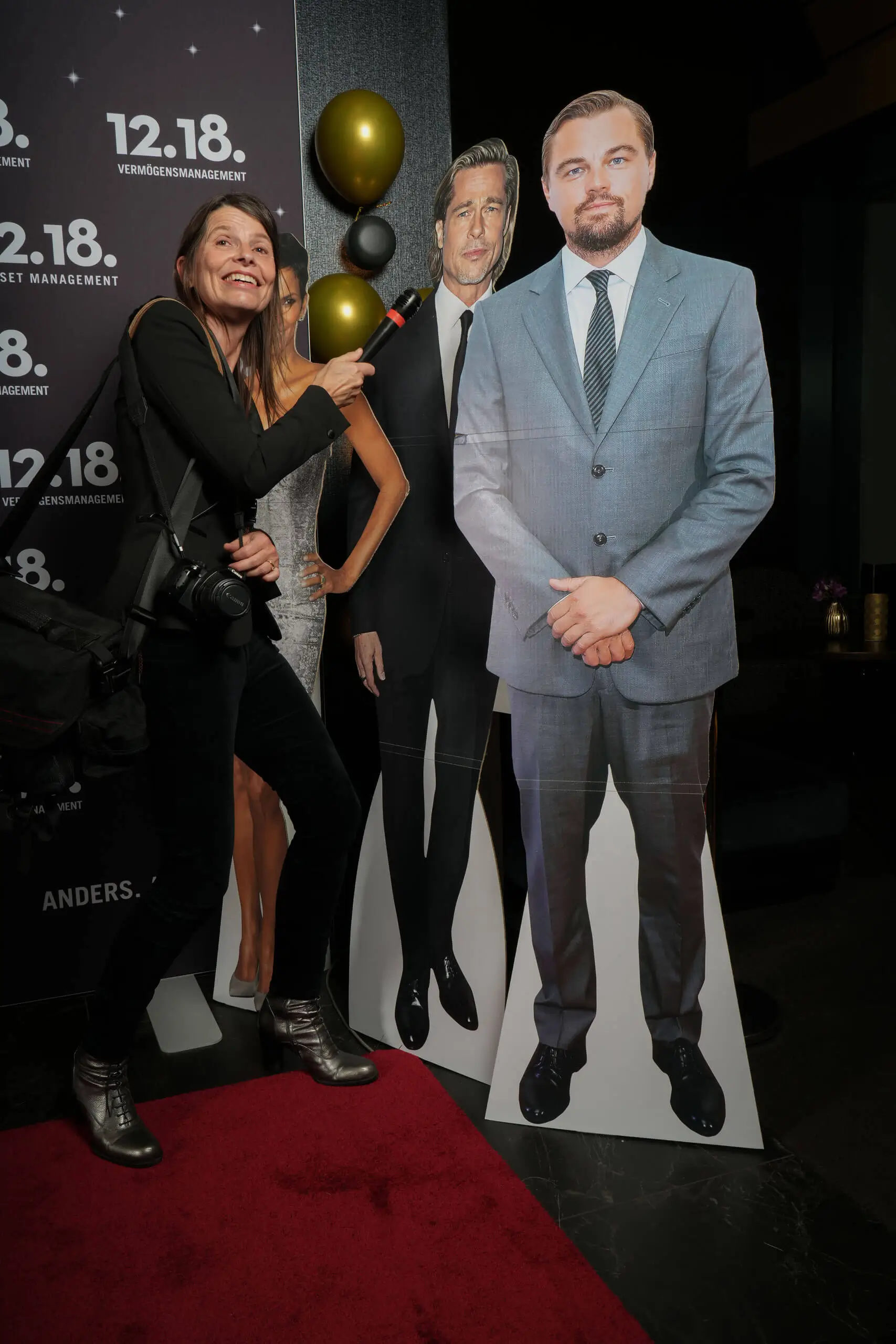 Eine Frau posiert verspielt mit Pappaufstellern von Brad Pitt und Leonardo DiCaprio bei einer Veranstaltung.