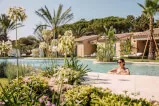 Woman sitting in a pool at 7Pines Resort Sardinia surrounded by palm trees and the outdoors