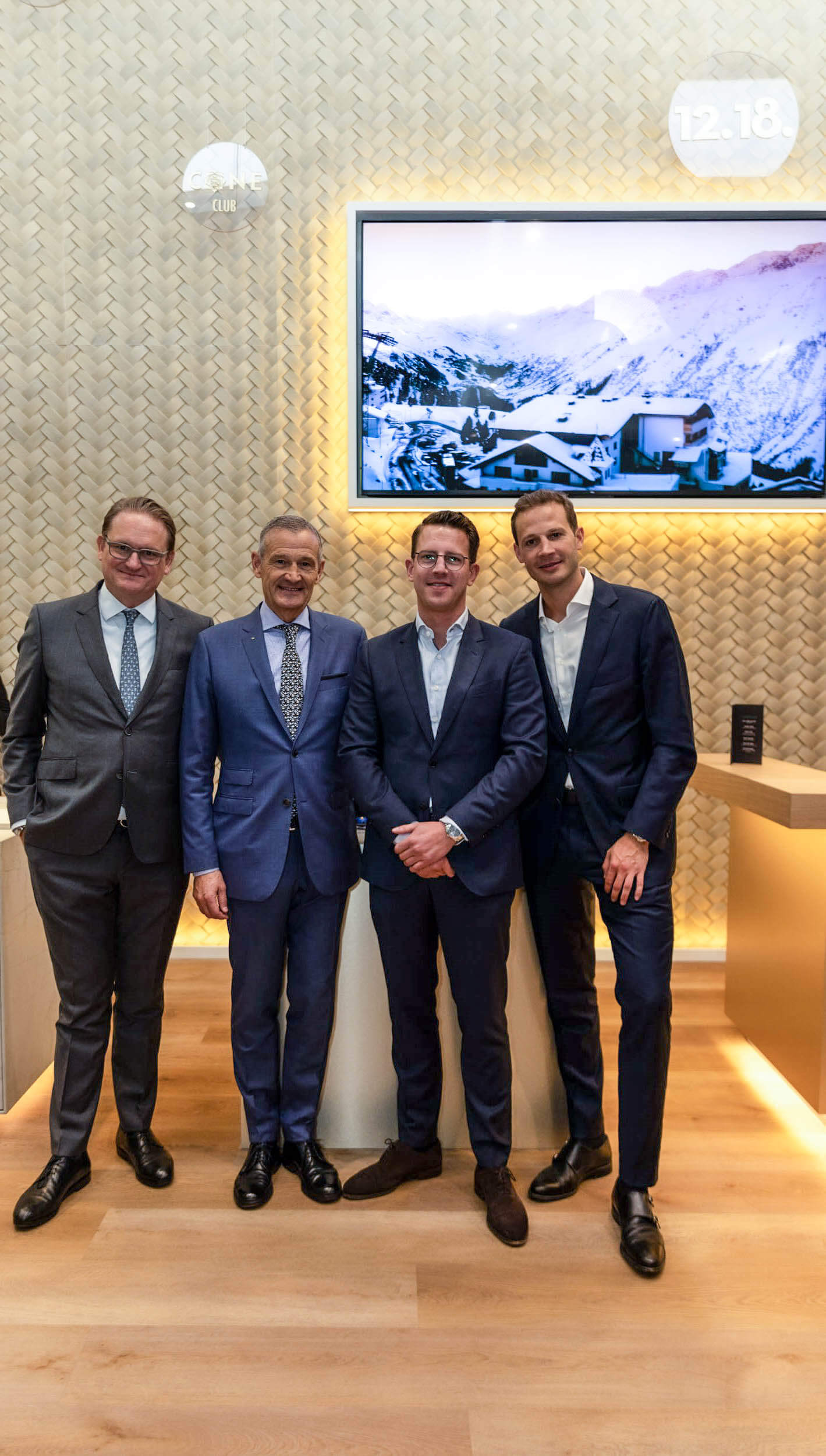 Gruppe von vier Männern in Anzügen, die in einem modernen Innenraum mit Schnee-Landschafts-Display posieren.