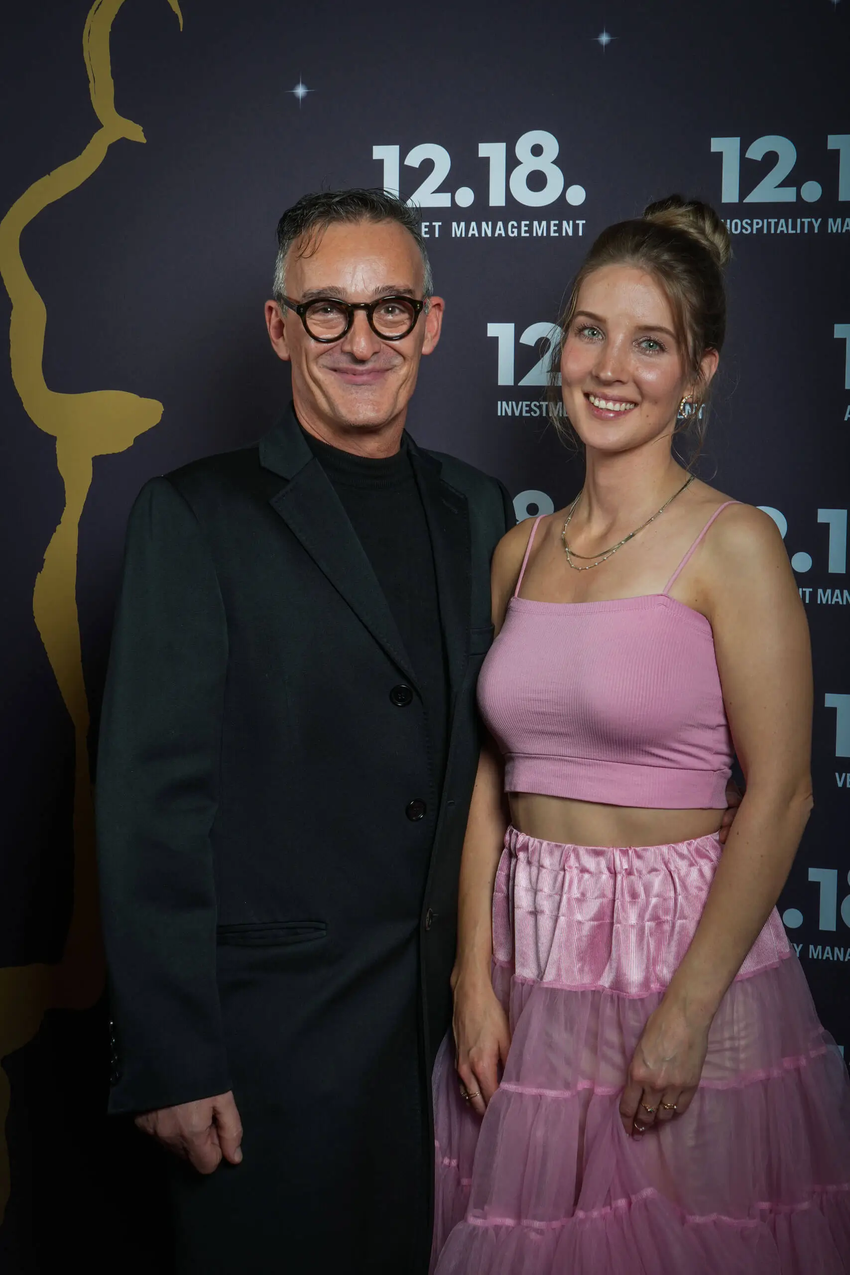 Ein stilvolles Paar beim Event von 12.18, mit einem Mann in Schwarz und einer Frau in Pink.
