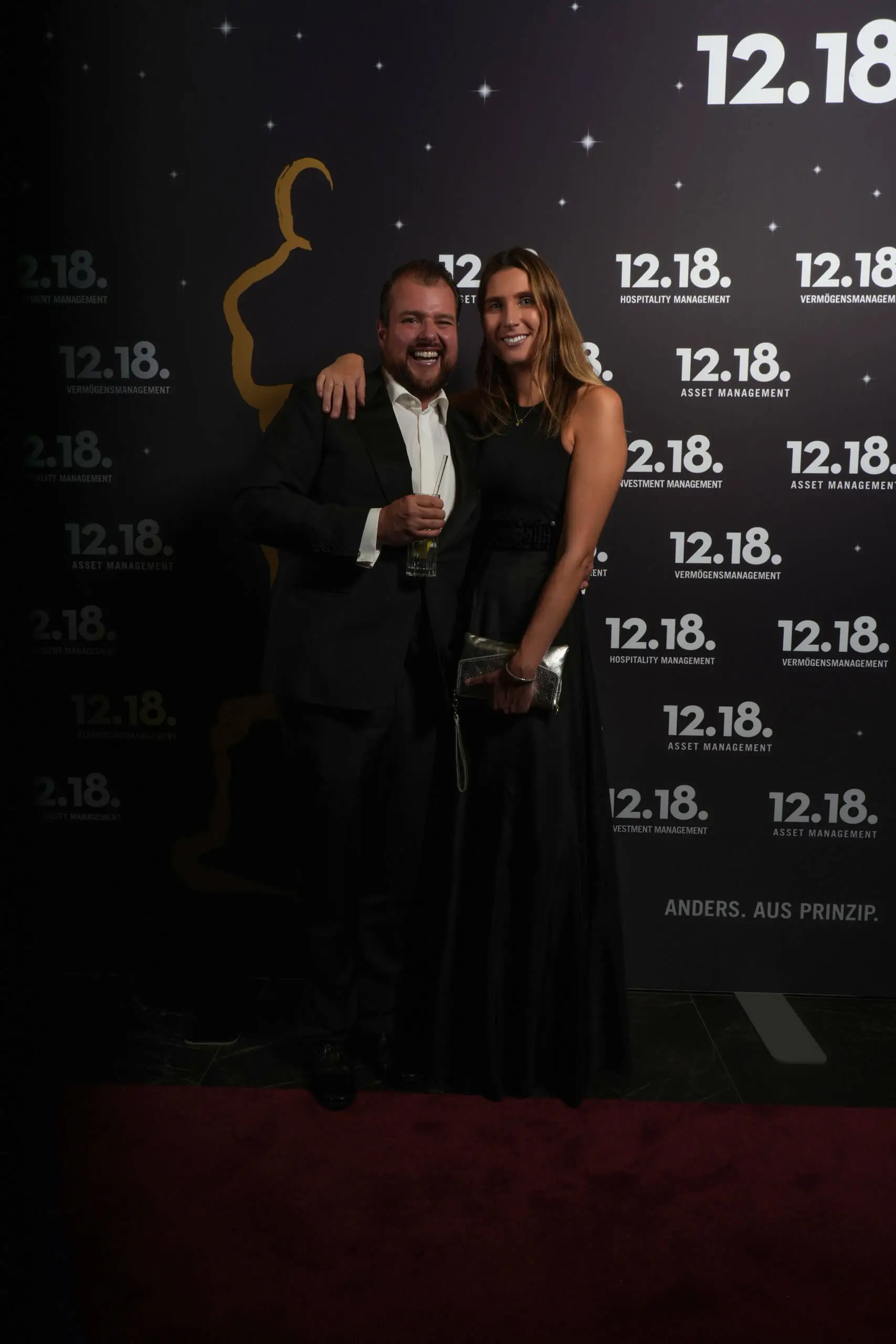 Ein Mann im Smoking und eine Frau in einem schwarzen Kleid posieren bei einer Preisverleihung.