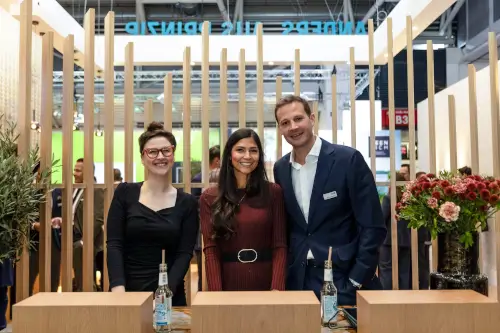 Mitarbeiter an einem professionellen Messestand, der Produkte einschließlich Flaschenwasser präsentiert.