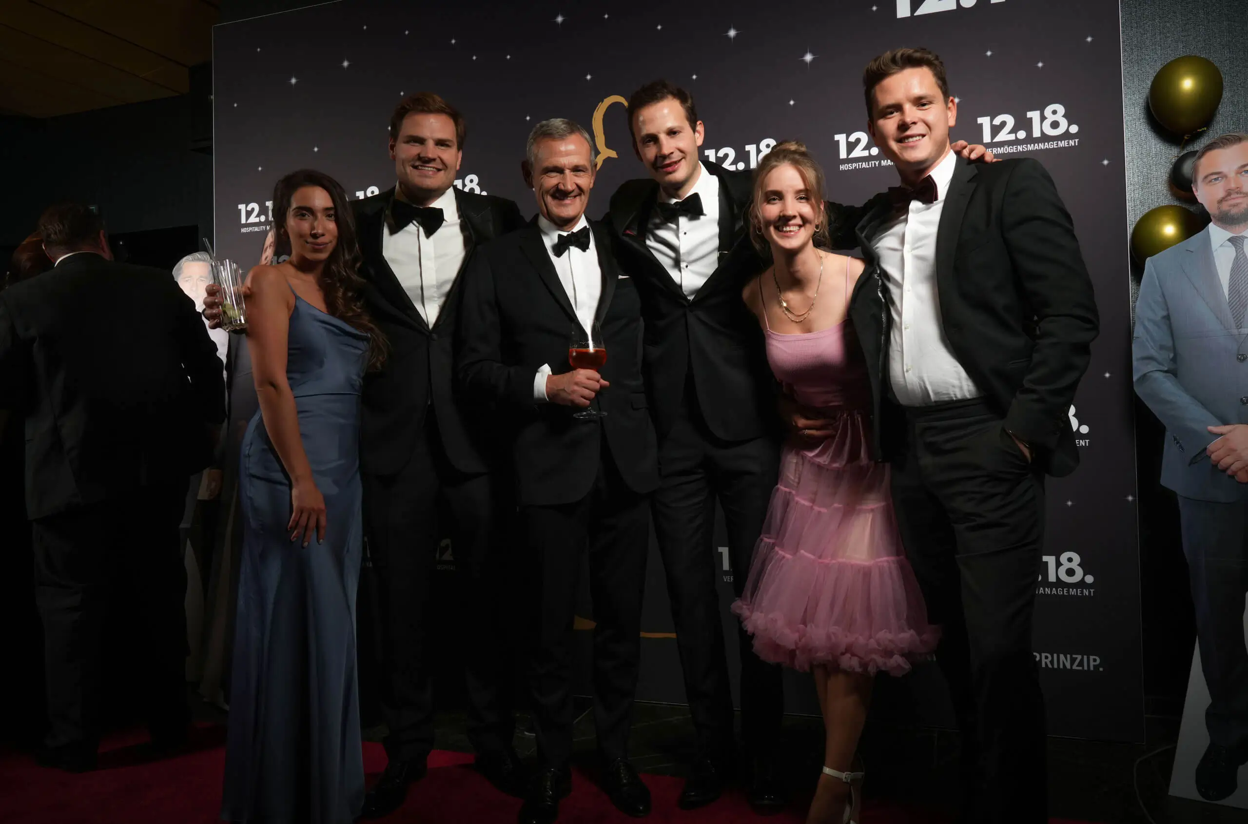 Elegante Gruppe bei einer Feier in Smoking und Abendkleidern.