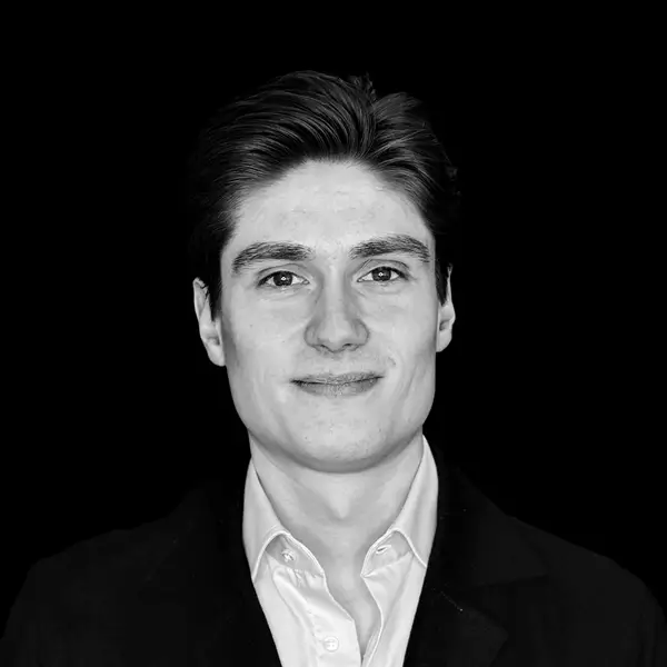 Portrait of a young man in a black suit against a black background.