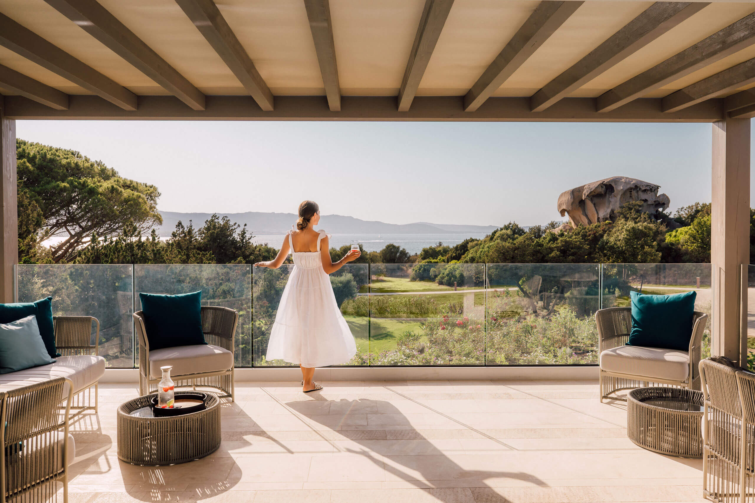 Eine Frau in weißem Kleid steht auf einer Terrasse mit Blick auf eine Landschaft, mit dem Kontext d