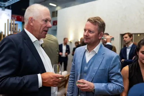 Zwei Männer in Anzügen diskutieren mit Gläsern bei einer Networking-Veranstaltung.