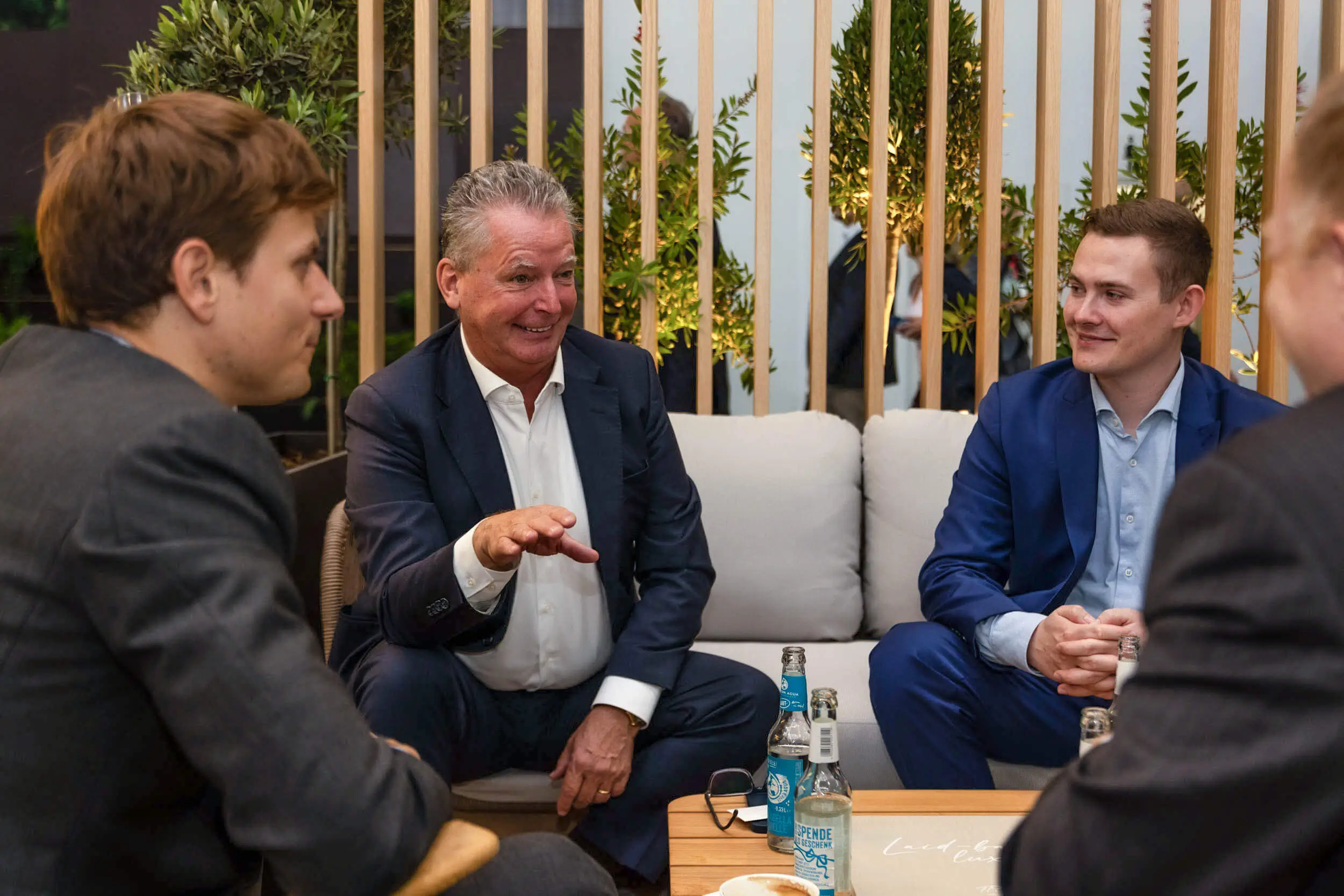 Männer im Anzug im Gespräch in einer modernen Lounge bei einem geschäftlichen Netzwerktreffen.