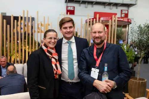 Drei Fachleute netzwerken auf einer Veranstaltung, mit stilvollen Loungemöbeln im Hintergrund.