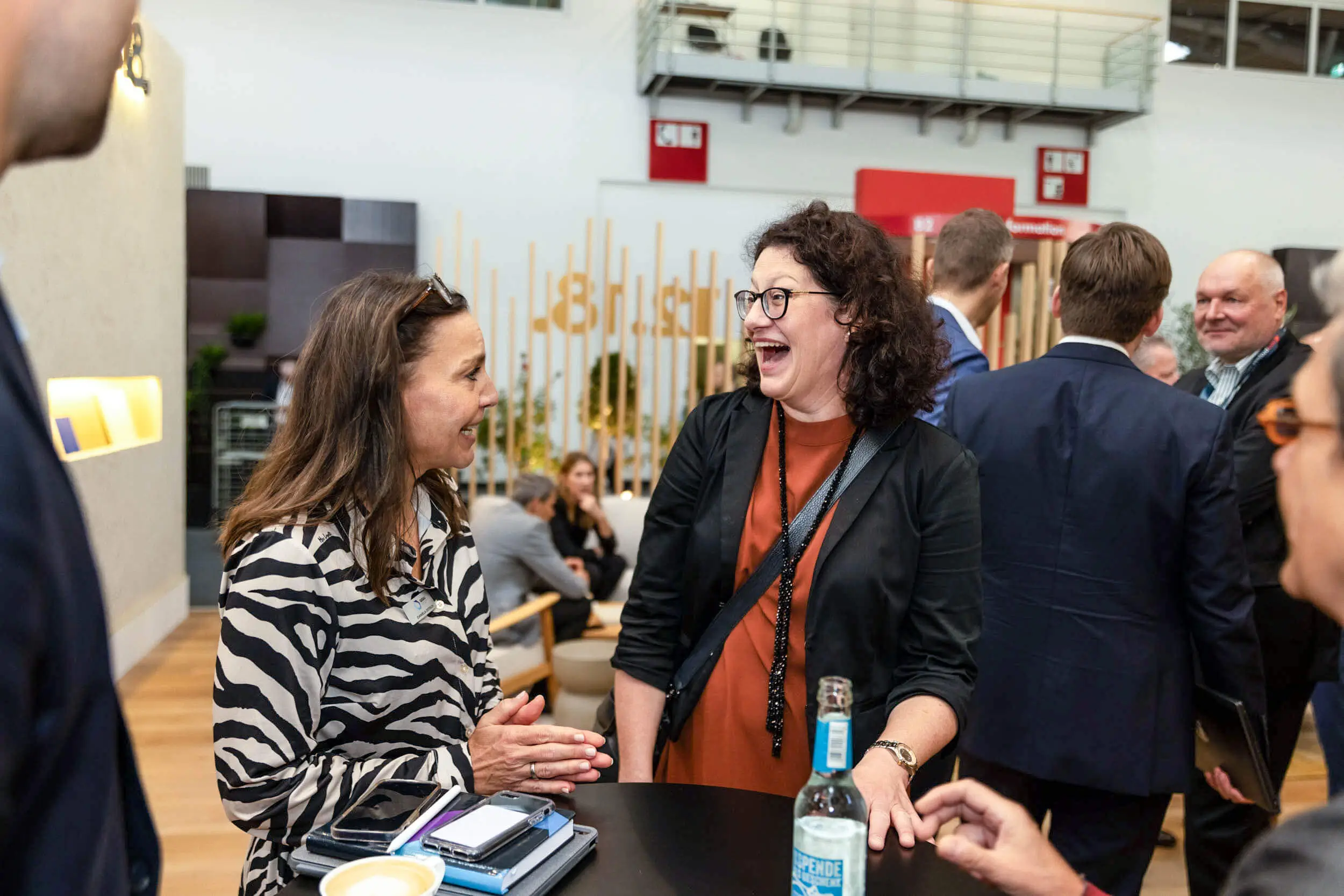 Zwei Frauen unterhalten sich lachend beim Networking auf einer Messe.