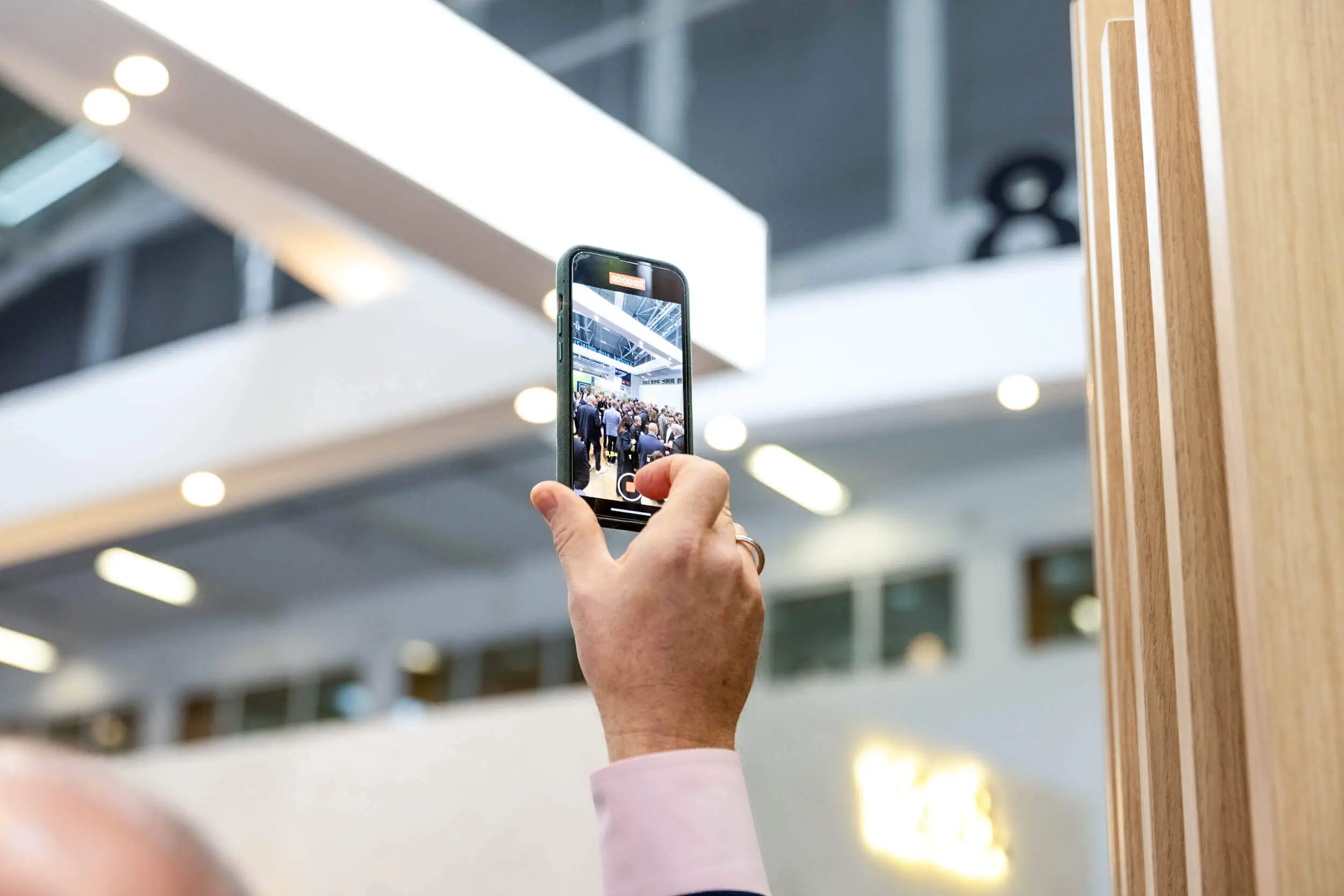 Eine Person, die mit einem Smartphone ein Foto von einer Menschenmenge in einem modernen Ausstellungszentrum macht.
