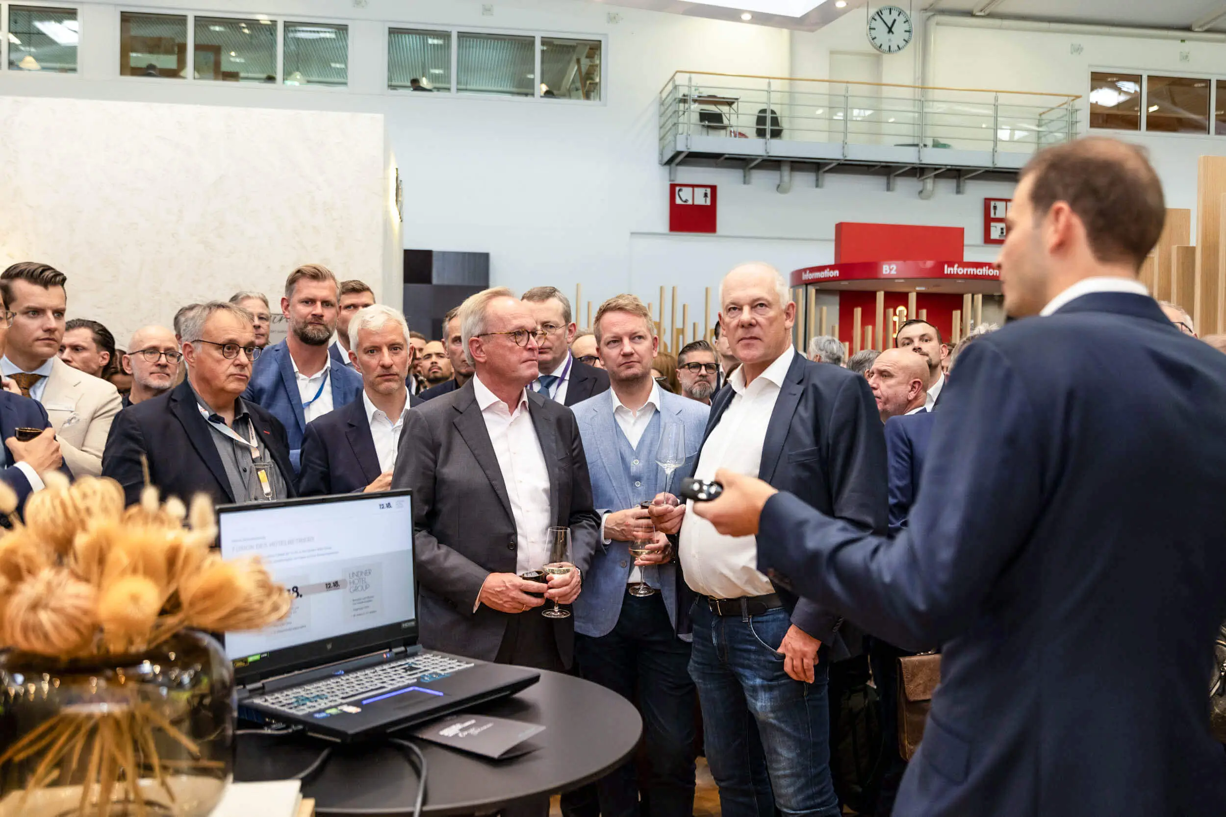 Eine Gruppe von Männern verfolgt eine Präsentation an einem Messestand.