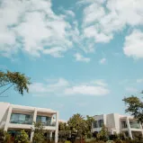 Eine Gruppe weißer Gebäude mit Bäumen und blauem Himmel symbolisiert die außergewöhnlichen Immobilien im Portfolio.