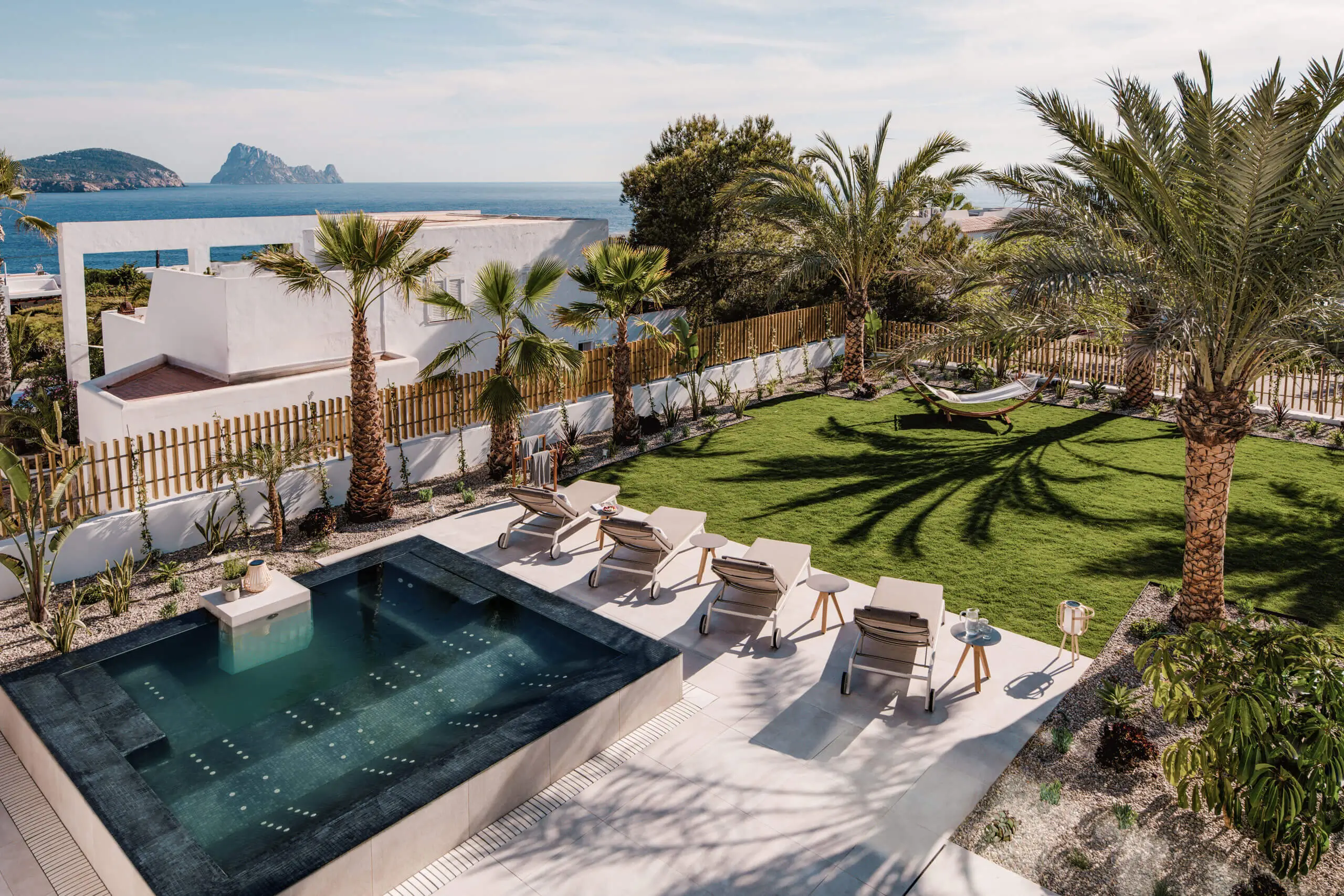 Ein luxuriöser Poolbereich mit Liegen und Palmen mit Blick auf das Meer.