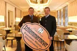 Zwei Männer präsentieren das Schlemmermeyer-Schild in einer eleganten Restaurant-Umgebung.