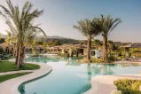 A relaxing outdoor pool area with palm trees and buildings in a tranquil spa town setting, creating a serene environment for leisure and escape. Property investment and management by 12. 18. Investment Management GmbH. Visit website for more information: 12-18.com
